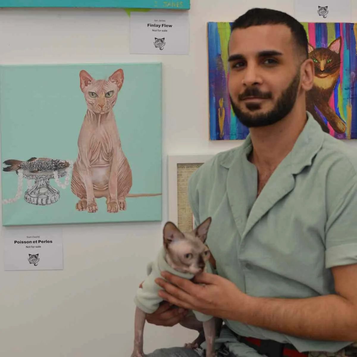 Man poses with his cat next to a painting of his cat