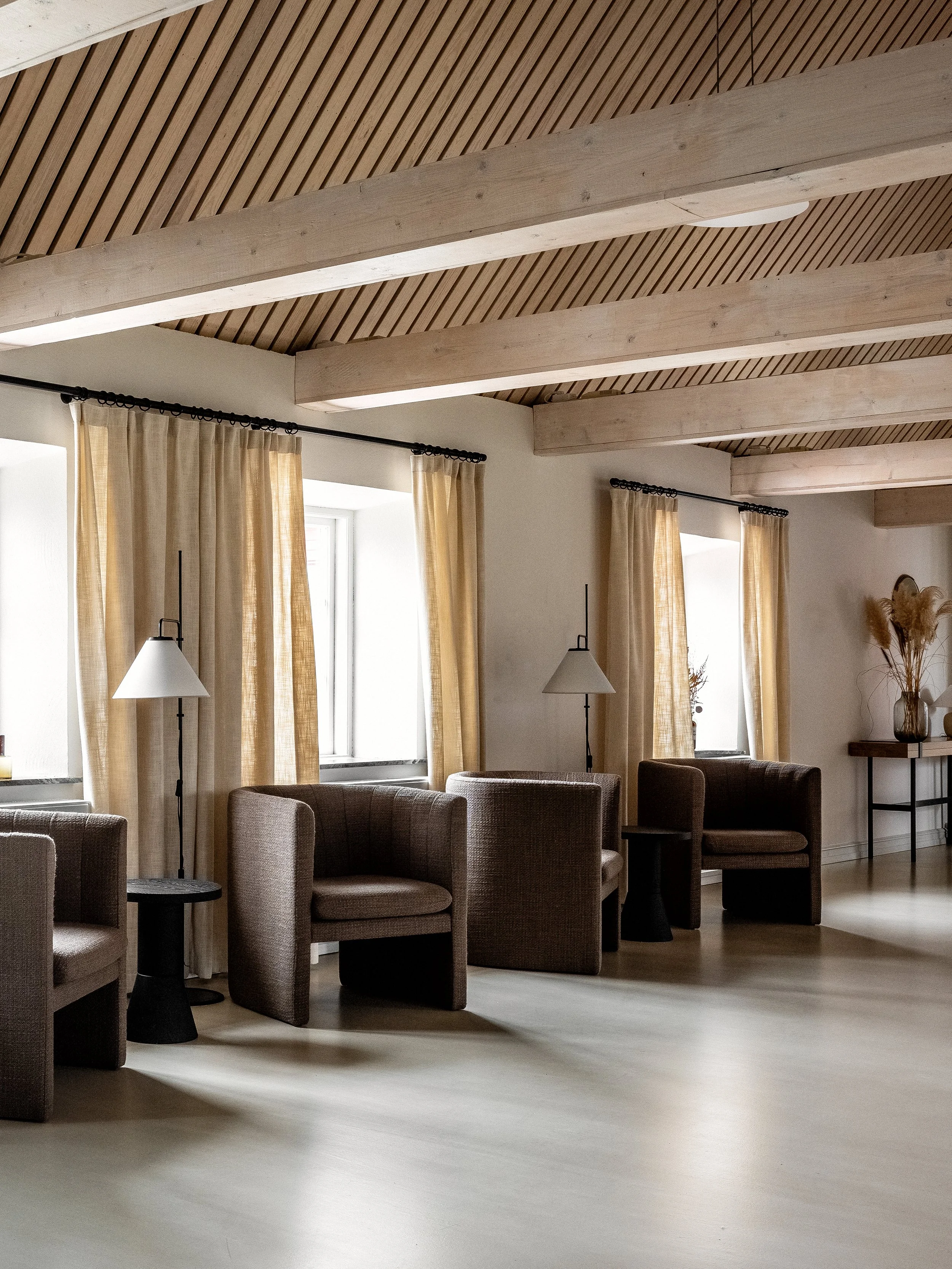 Fåtöljer i brunt tyg, synliga balkar i taket.