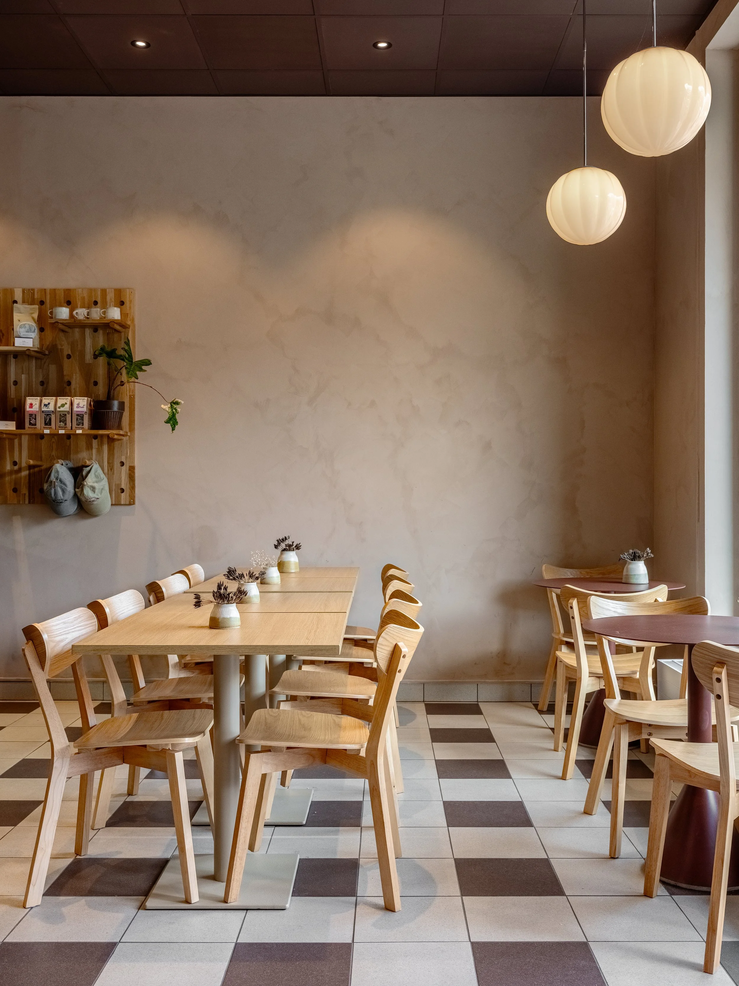 Sittplatser med träbord och stolar, ljusa väggar, rutigt klinkergolv och pendelarmaturer.