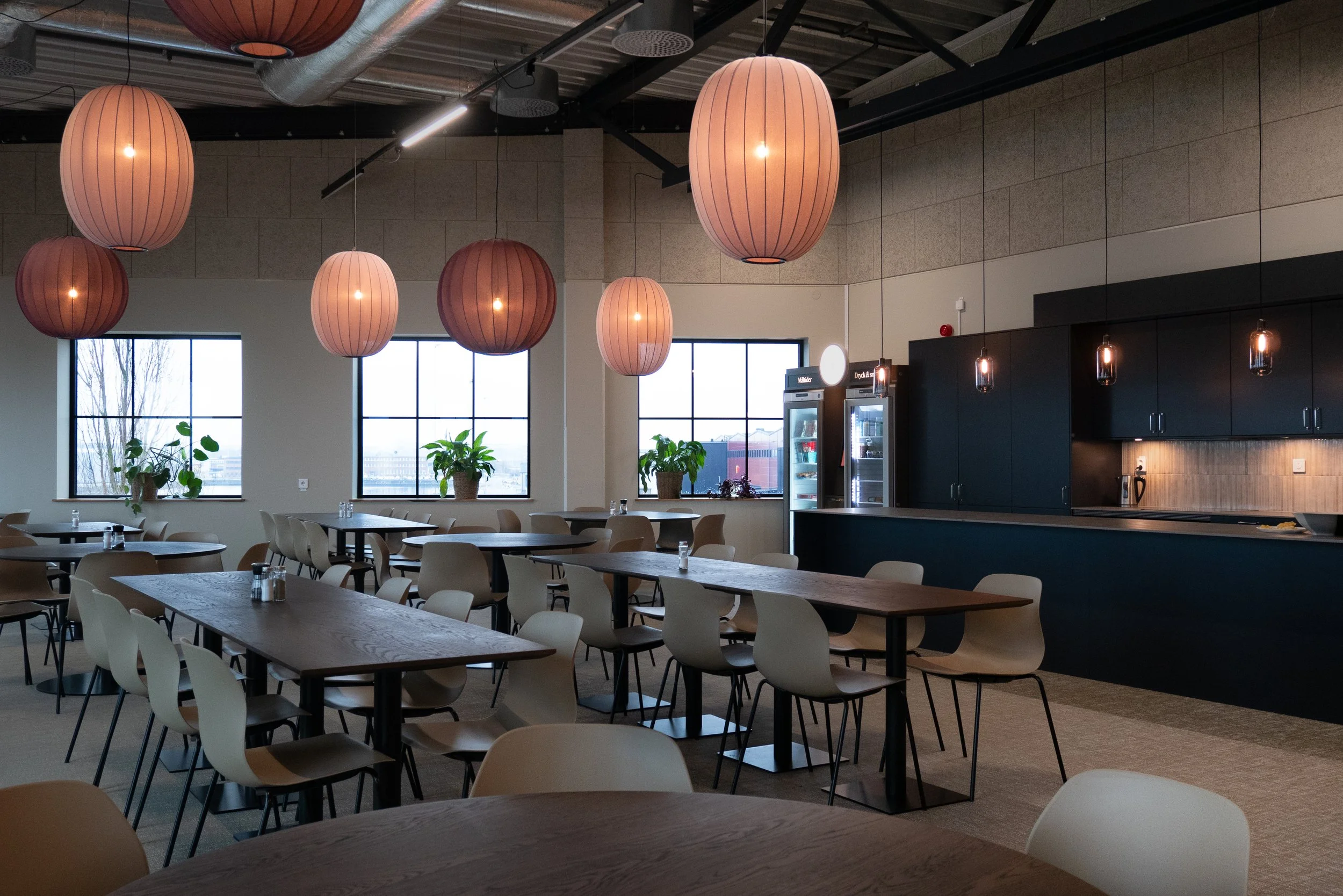Gemensam matsal med långbord, kök och stora pendellampor
