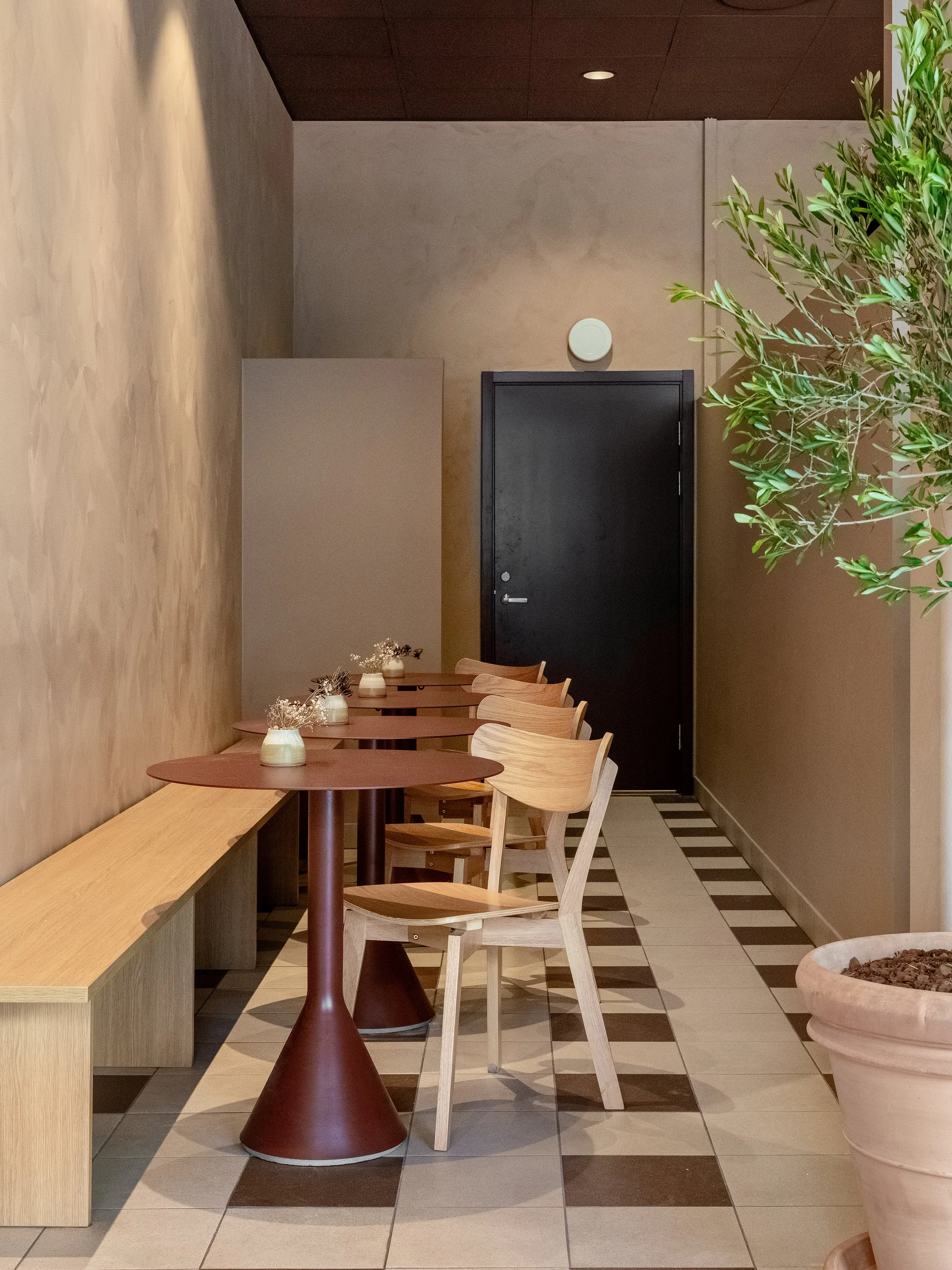 Seating area in the bakery with wooden chairs, round tables and a muted colour palette.