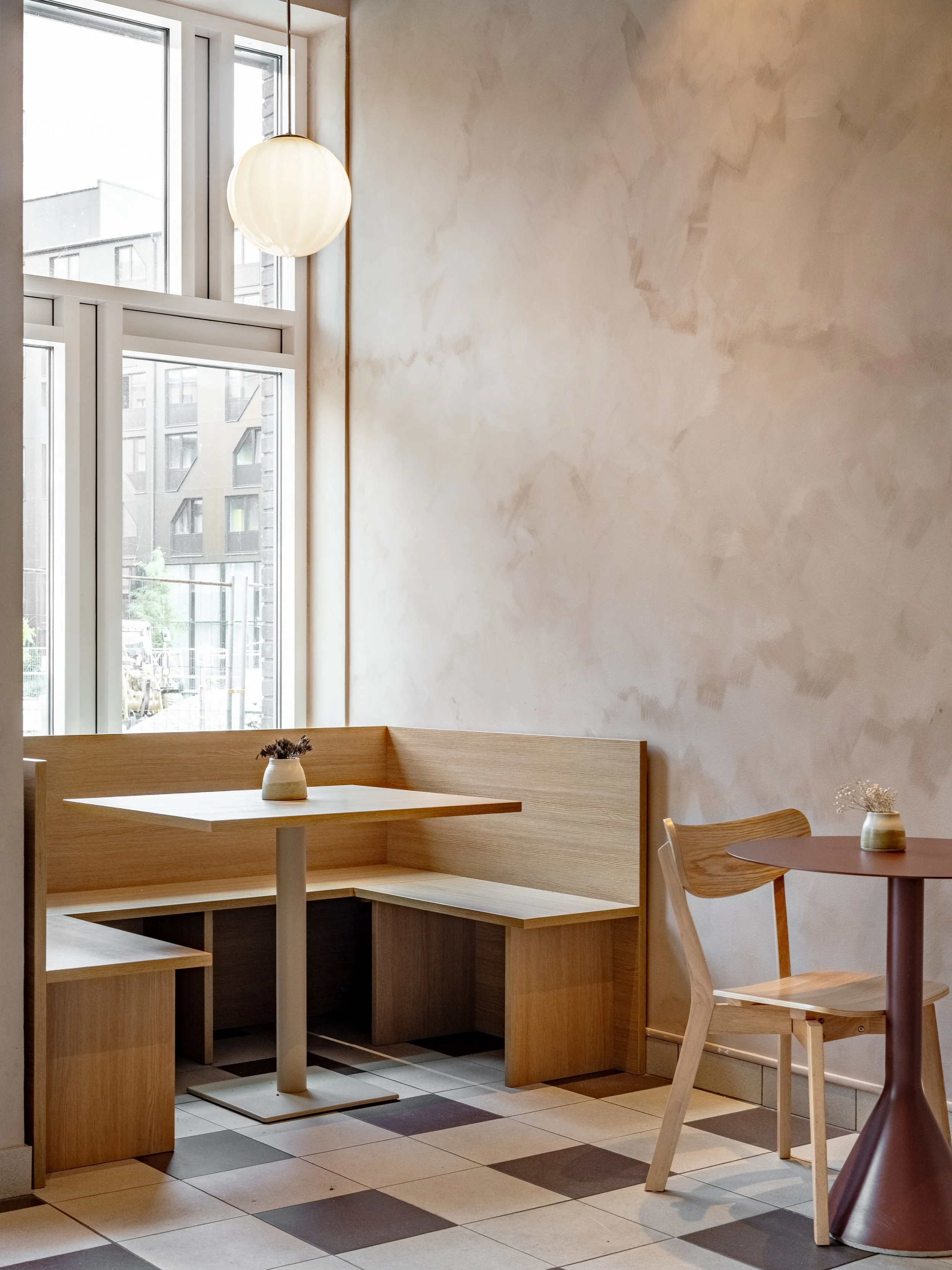 Built-in bench seating with wooden table and chairs next to a window, featuring pendant lighting, light walls and checkered tile flooring.