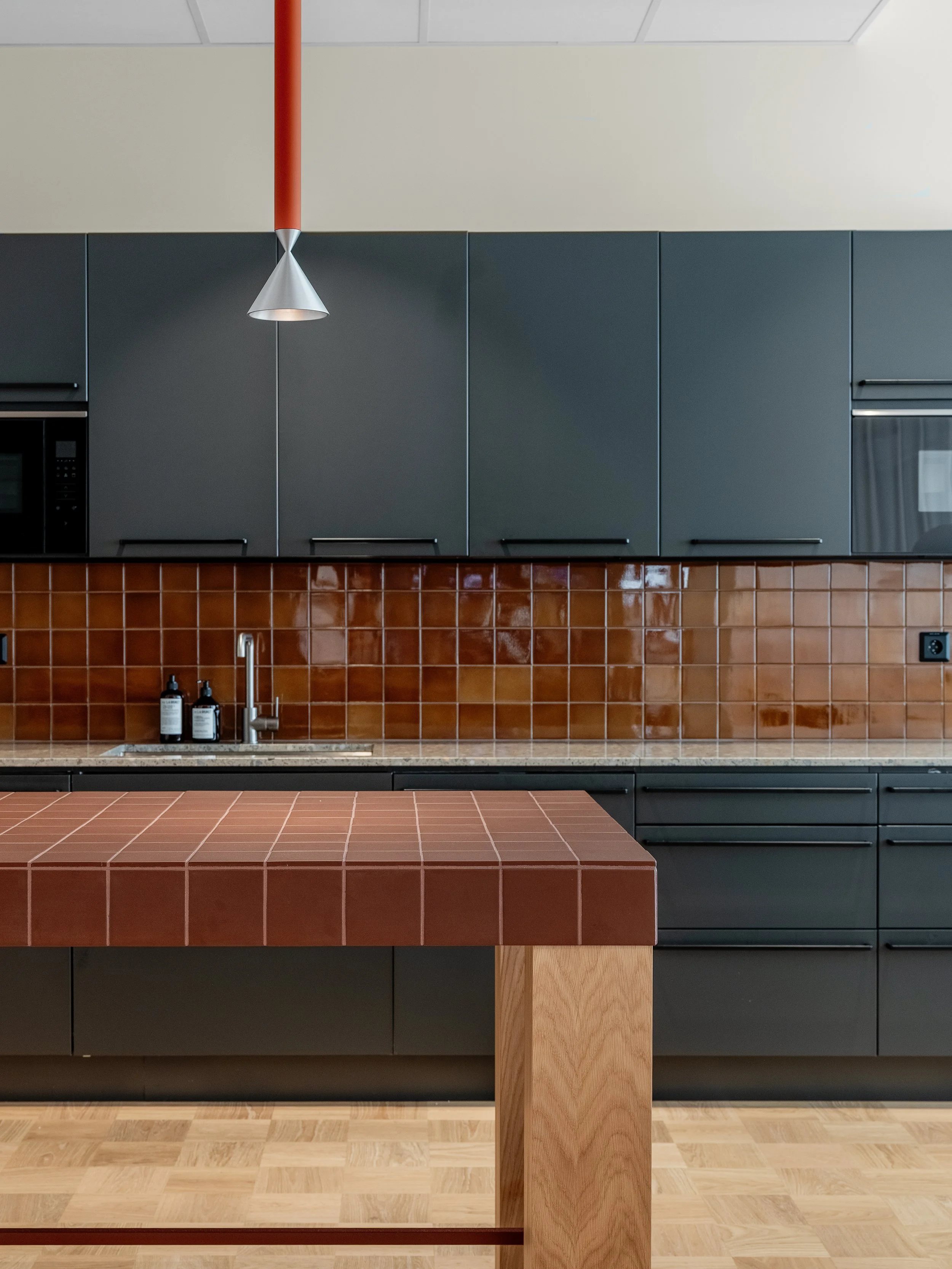 Detail of office kitchen with built-in kitchen island in brown tiles and dark cabinetry