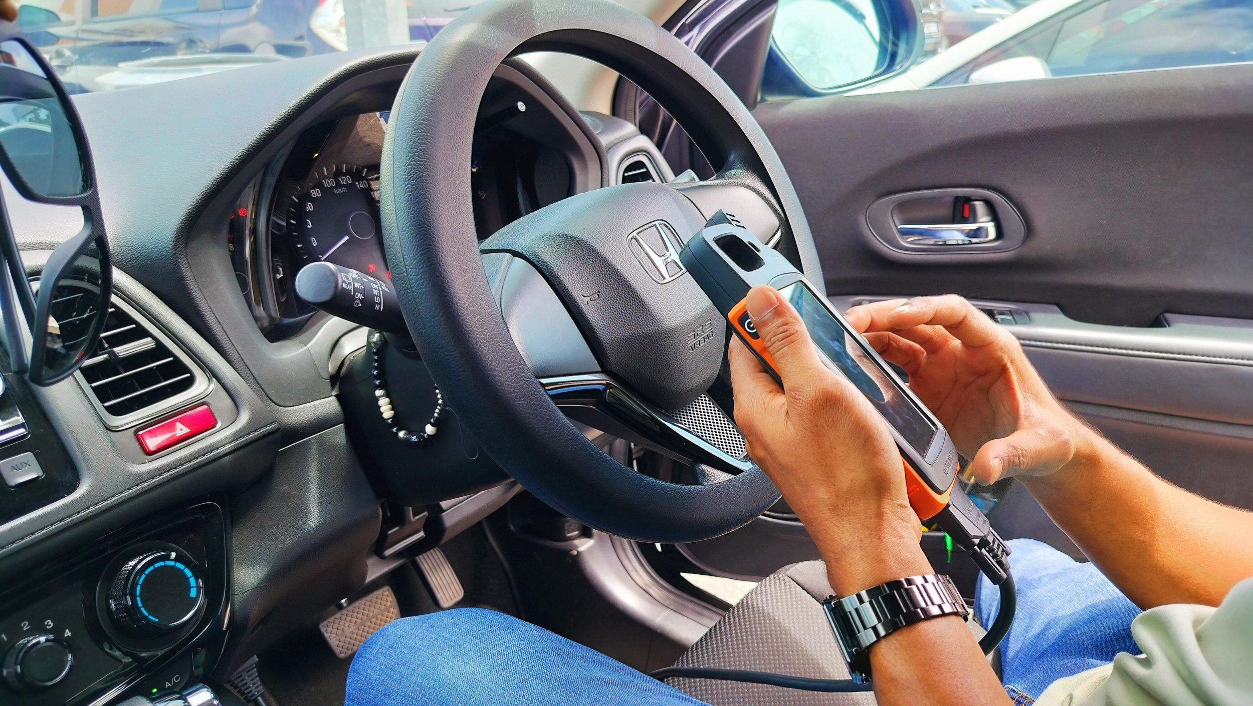 Person holding a testing device while sitting in the driver's seat of a Honda car.