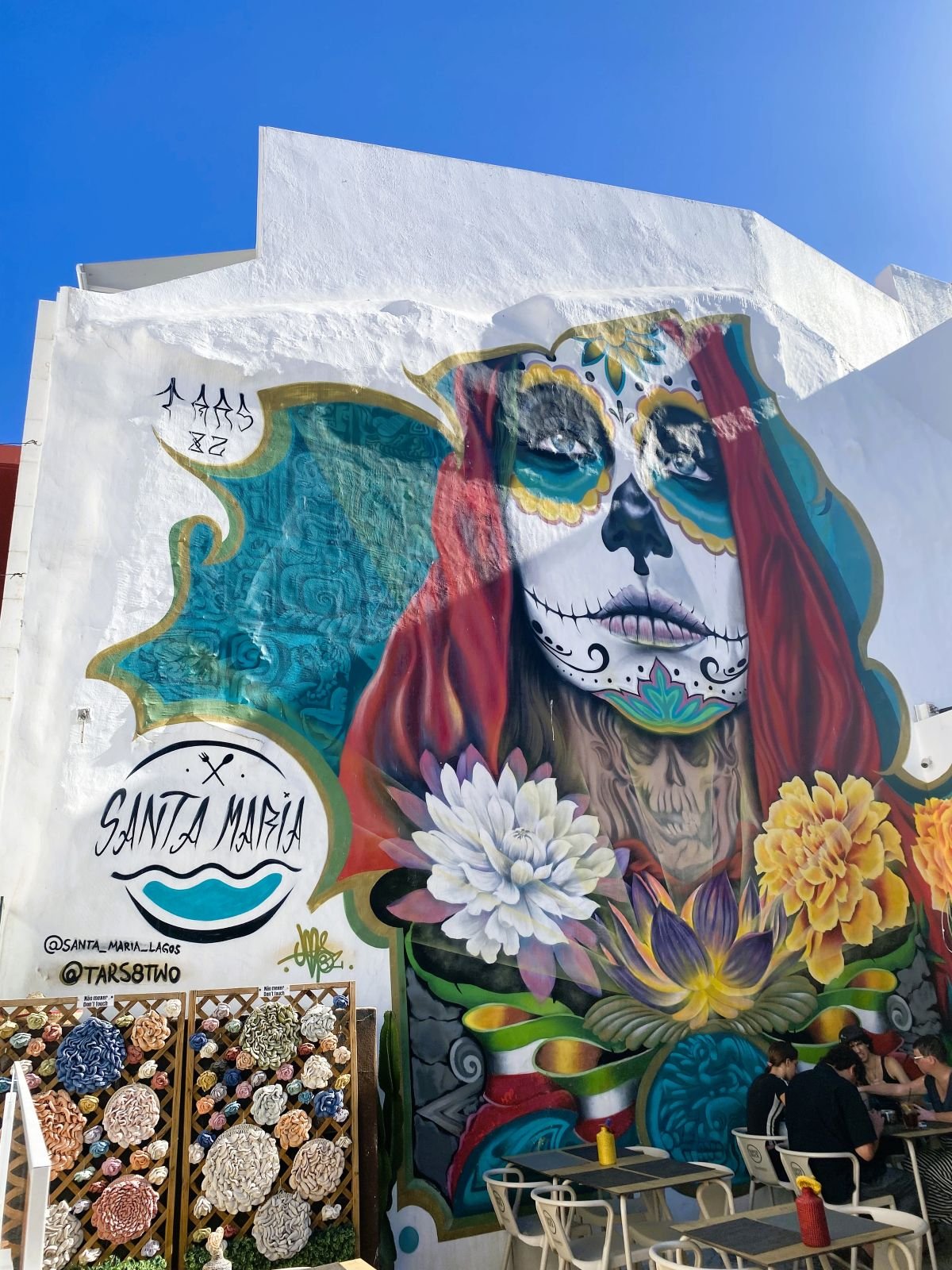 Farbenfrohe Street-Art mit großem Frauengesicht und Blumen an der Fassade des Restaurants Santa Maria in Lagos.