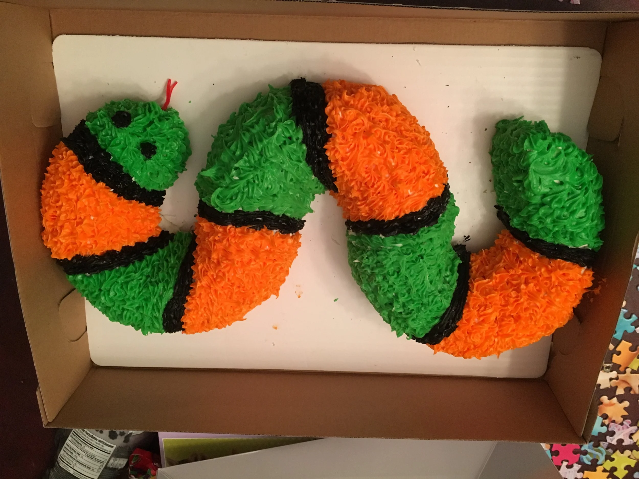 Two cupcakes decorated to resemble clownfish, with orange, green, and black frosting and a fish shape.