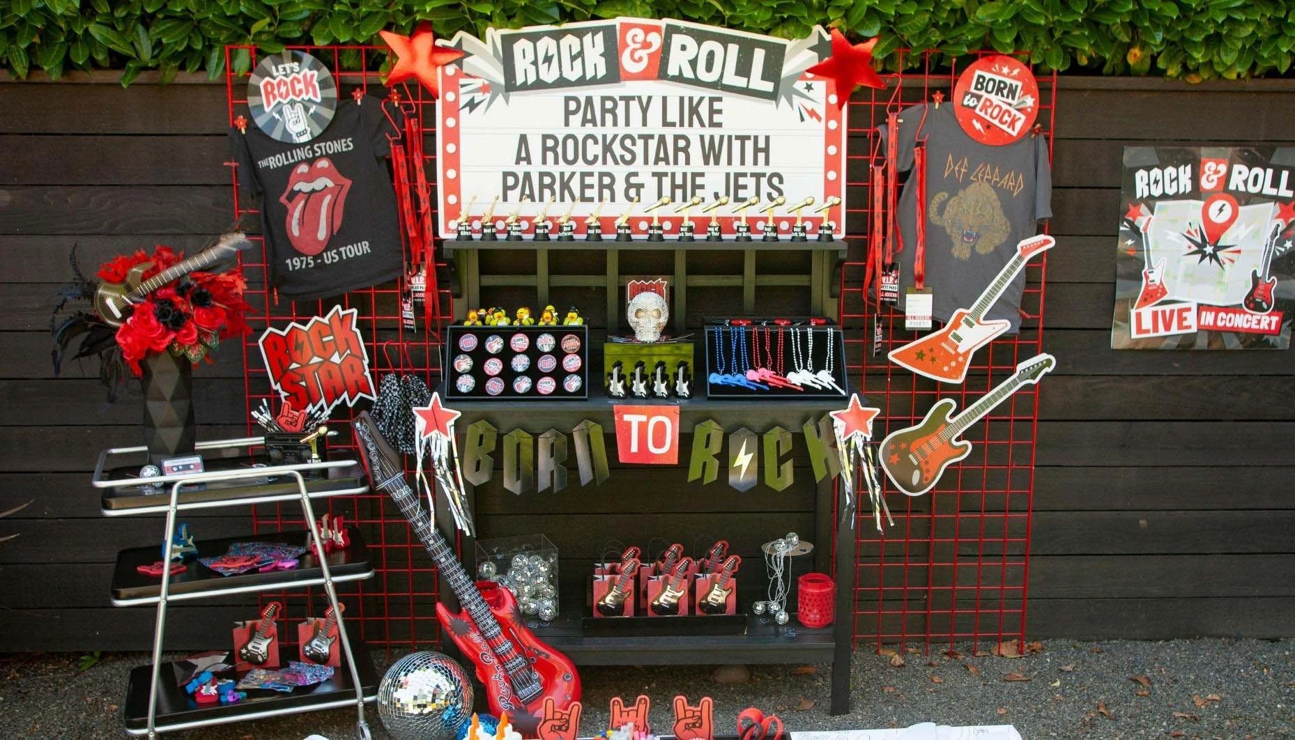 A rock and roll themed party setup with various decorations, T-shirts, acoustic guitars, and a sign that reads "Party like a rockstar with Parker & the Jets."
