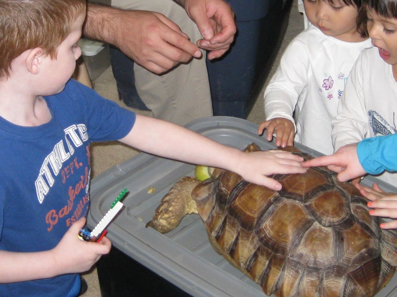 A glow-in-the-dark sensory table filled with colorful sand, foam cups, and small plastic balls, illuminated by purple and blue neon lights in a dark room.