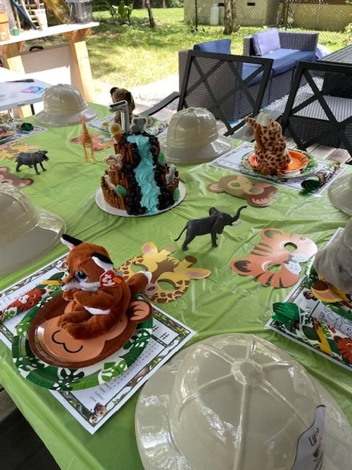 Safari-themed birthday party table with animal plush toys and decorations, set for children.