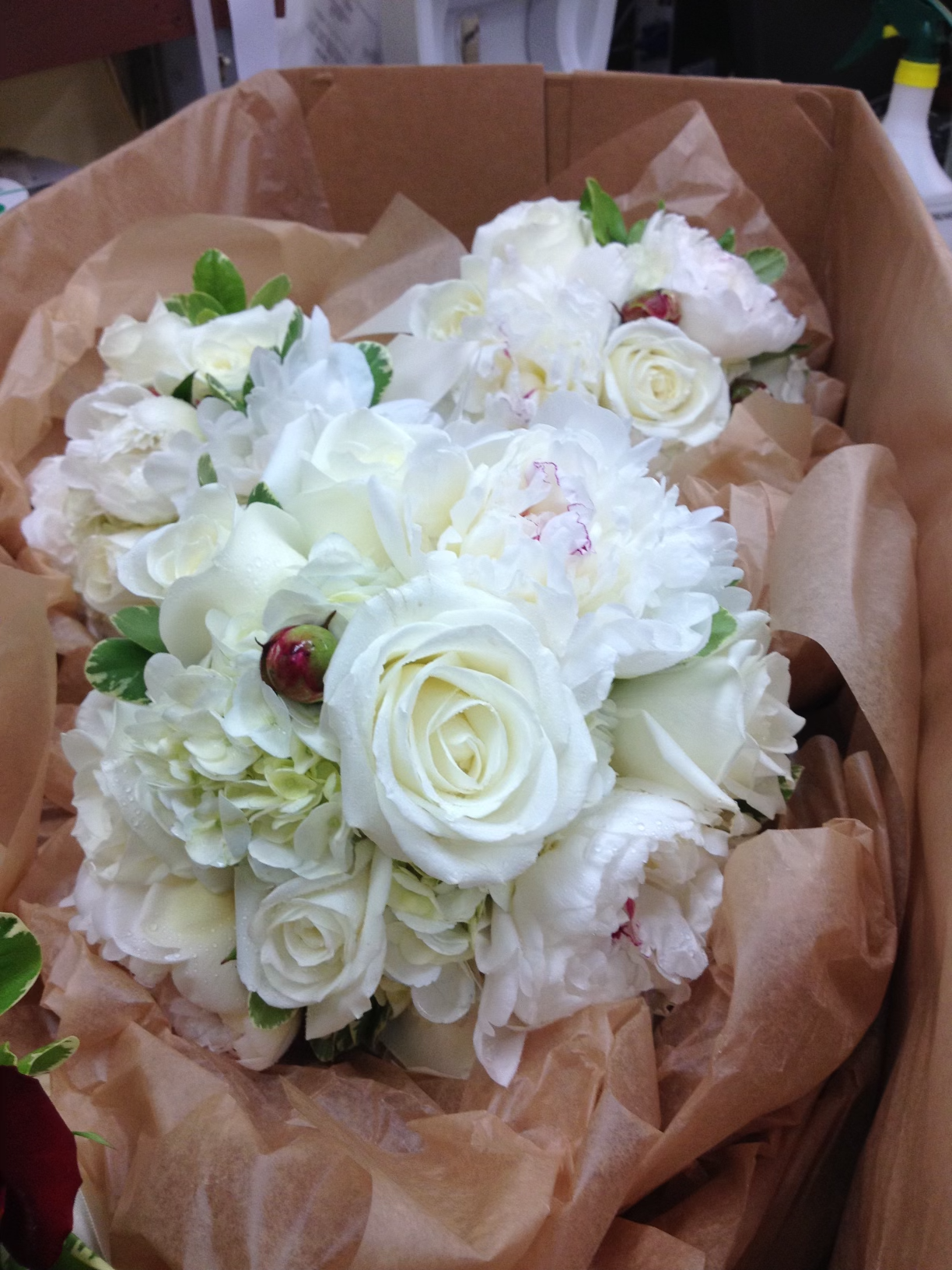 White rose and hydrangea bouquets in a cardboard box with brown paper wrapping.