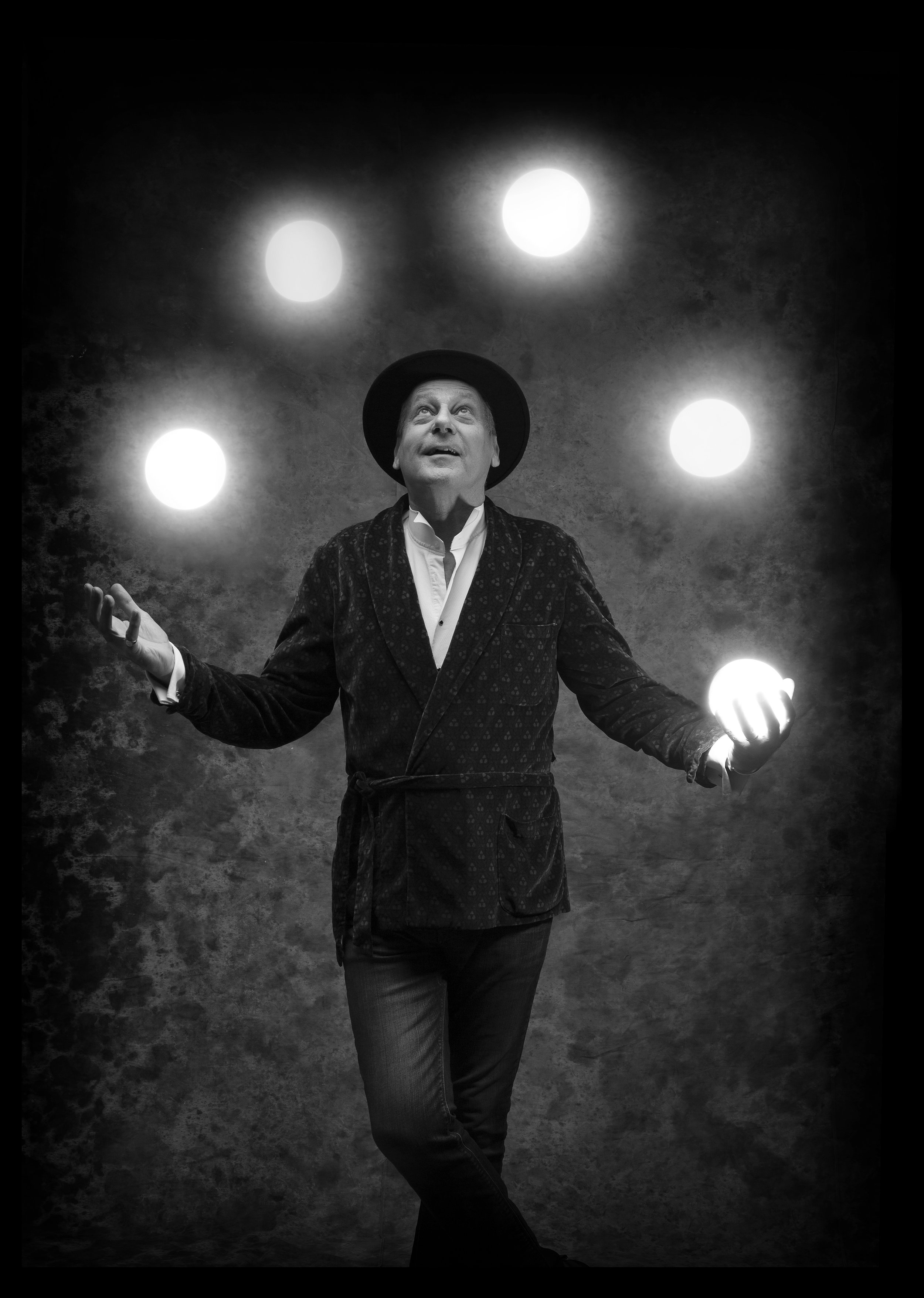 A photographer in a hat and blazer juggles with globes of light.
