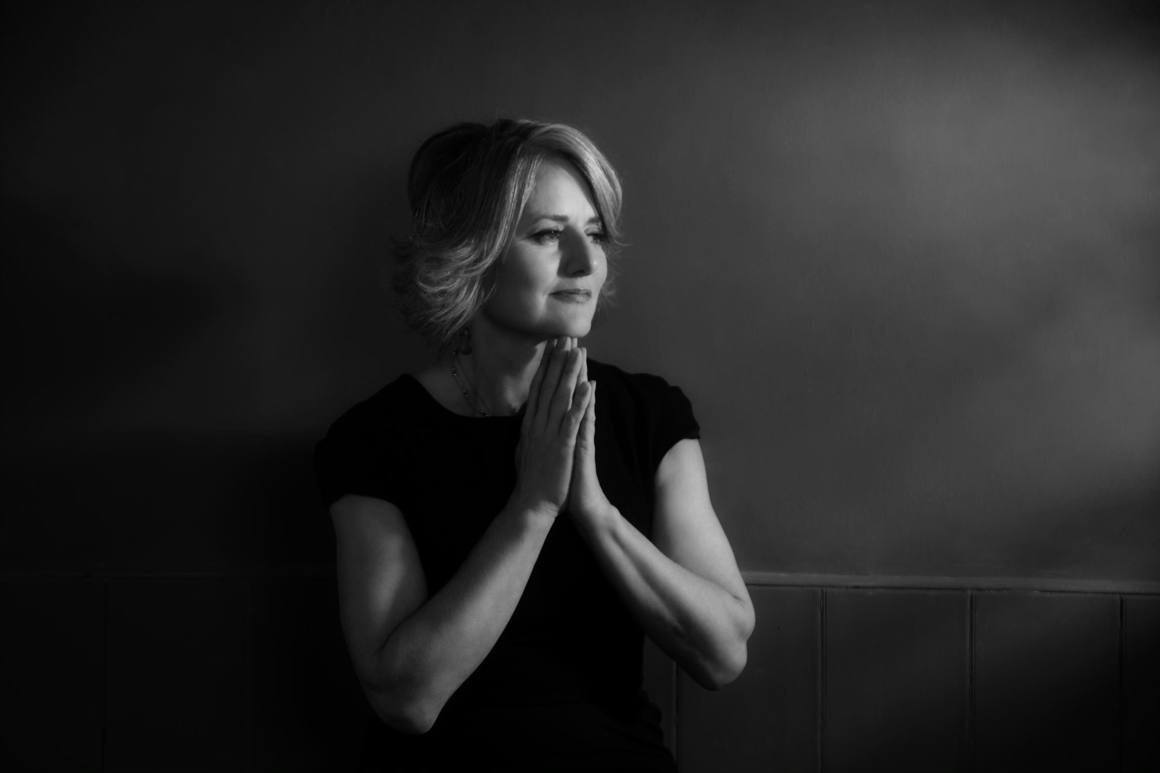 A woman holding her hands, as like in prayer, up to her face with a smile on her face.