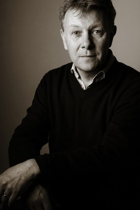 A man in a dark coloured top smiling in his headshot.