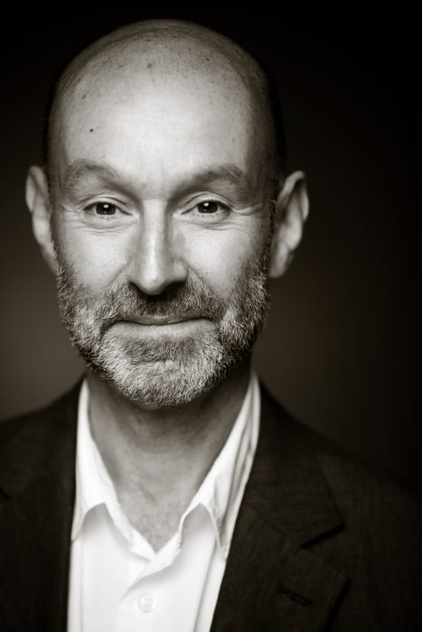 A man in a white shirt and suit slightly smiling at the camera.