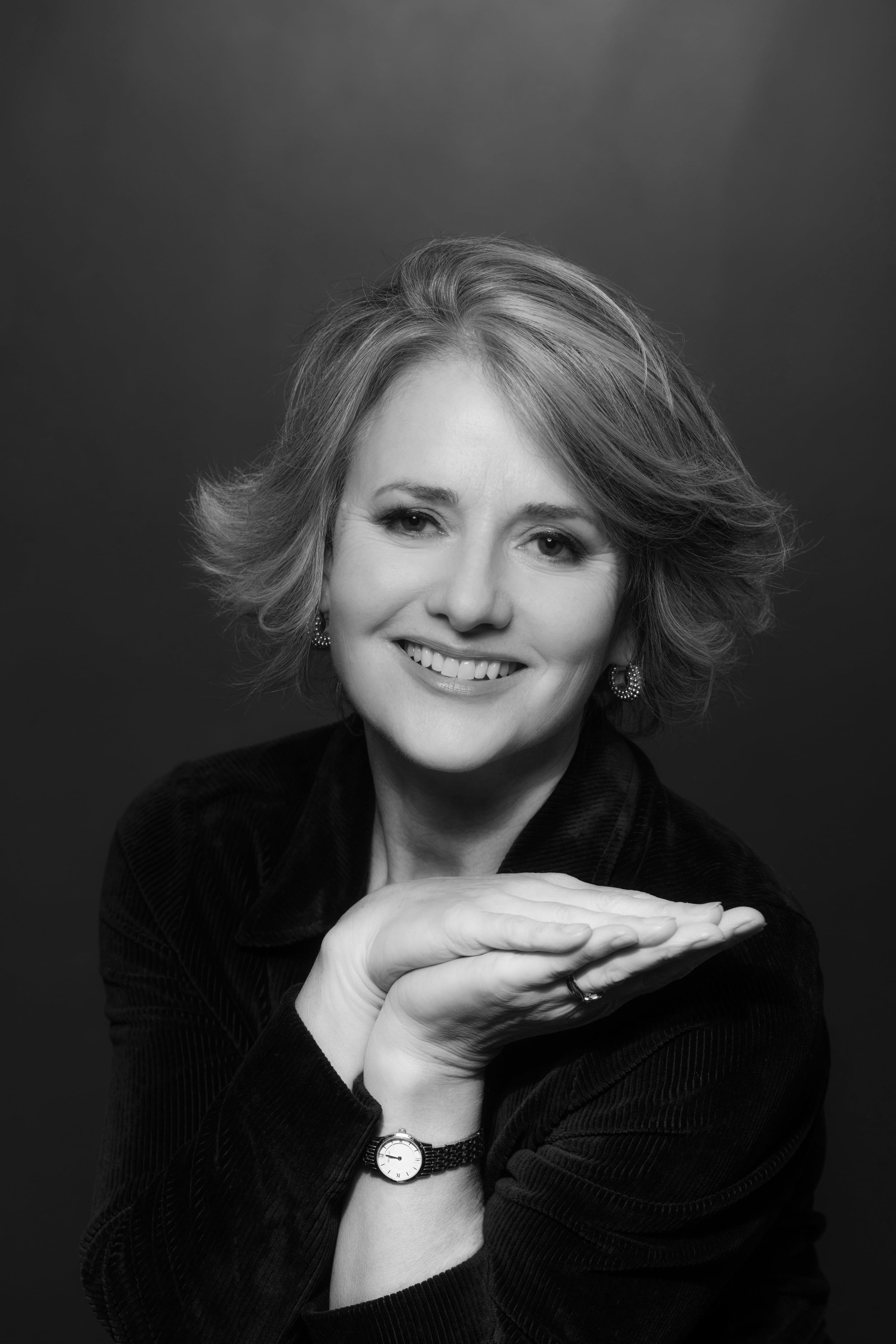 A woman has her hands clasped to the side and smiles.