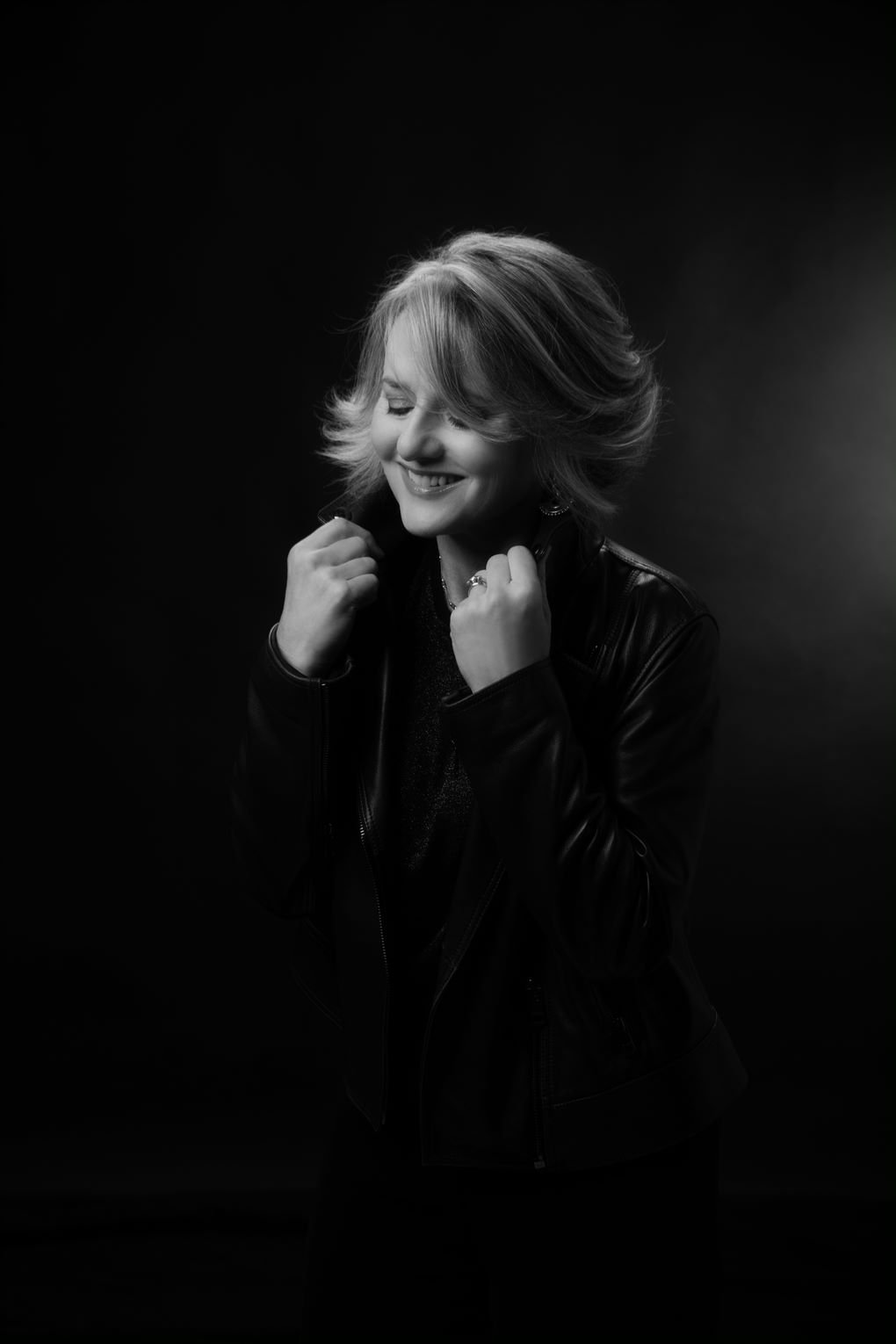 A woman holding the collar of her leather jacket in a black and white photo.