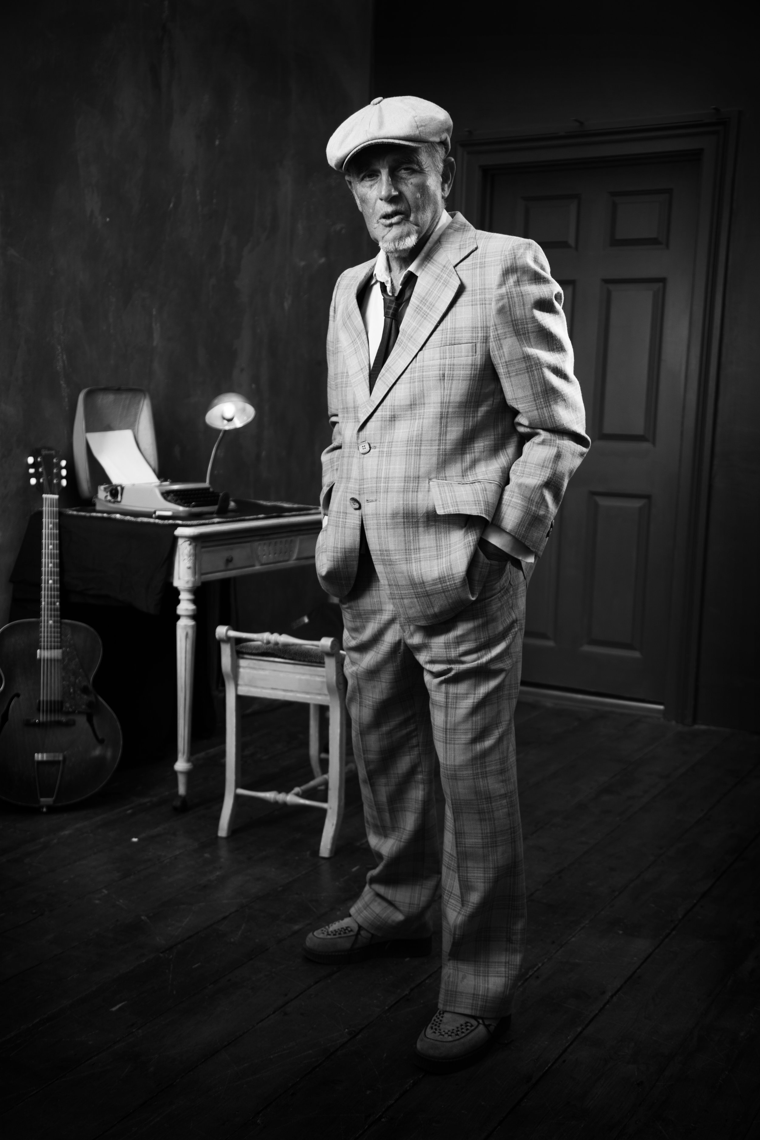 A creative photo of a man in front of a writing desk. He is wearing a suit and hat.