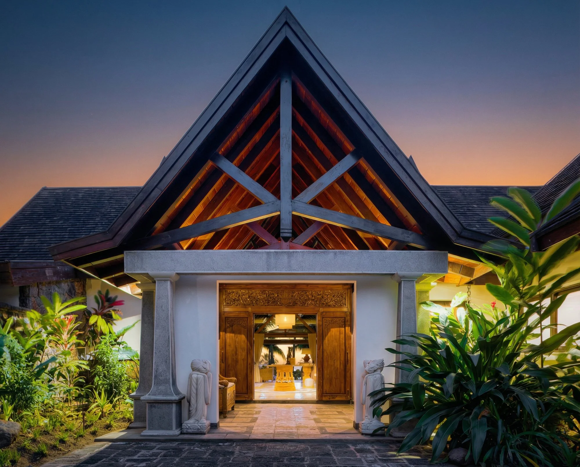 Une architecture de maison moderne avec un toit en pente en bois, entourée de végétation luxuriante, ouverte sur l'intérieur avec un couloir bien éclairé.