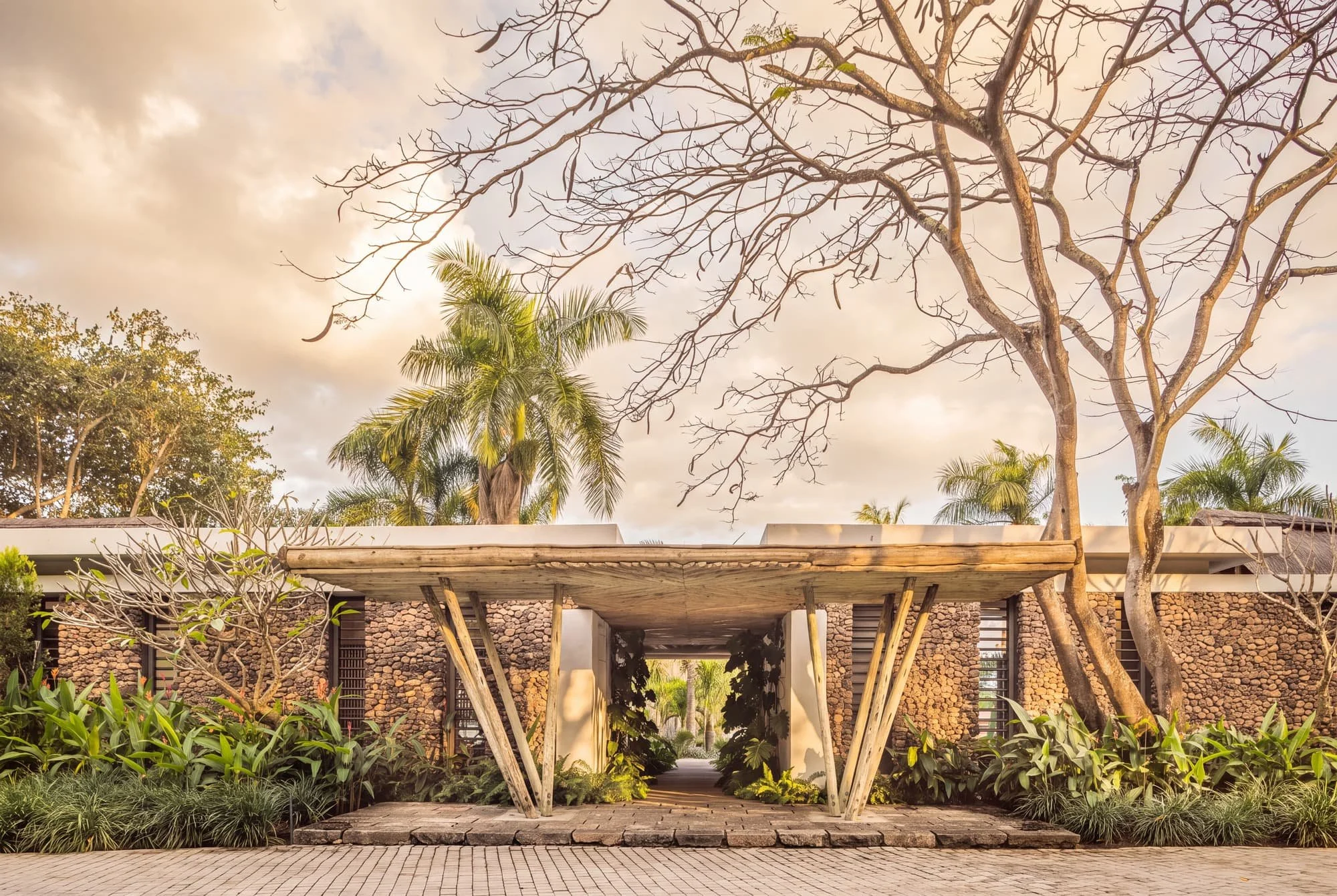 Timber entrance pergola framed by stone walls and mature tropical trees