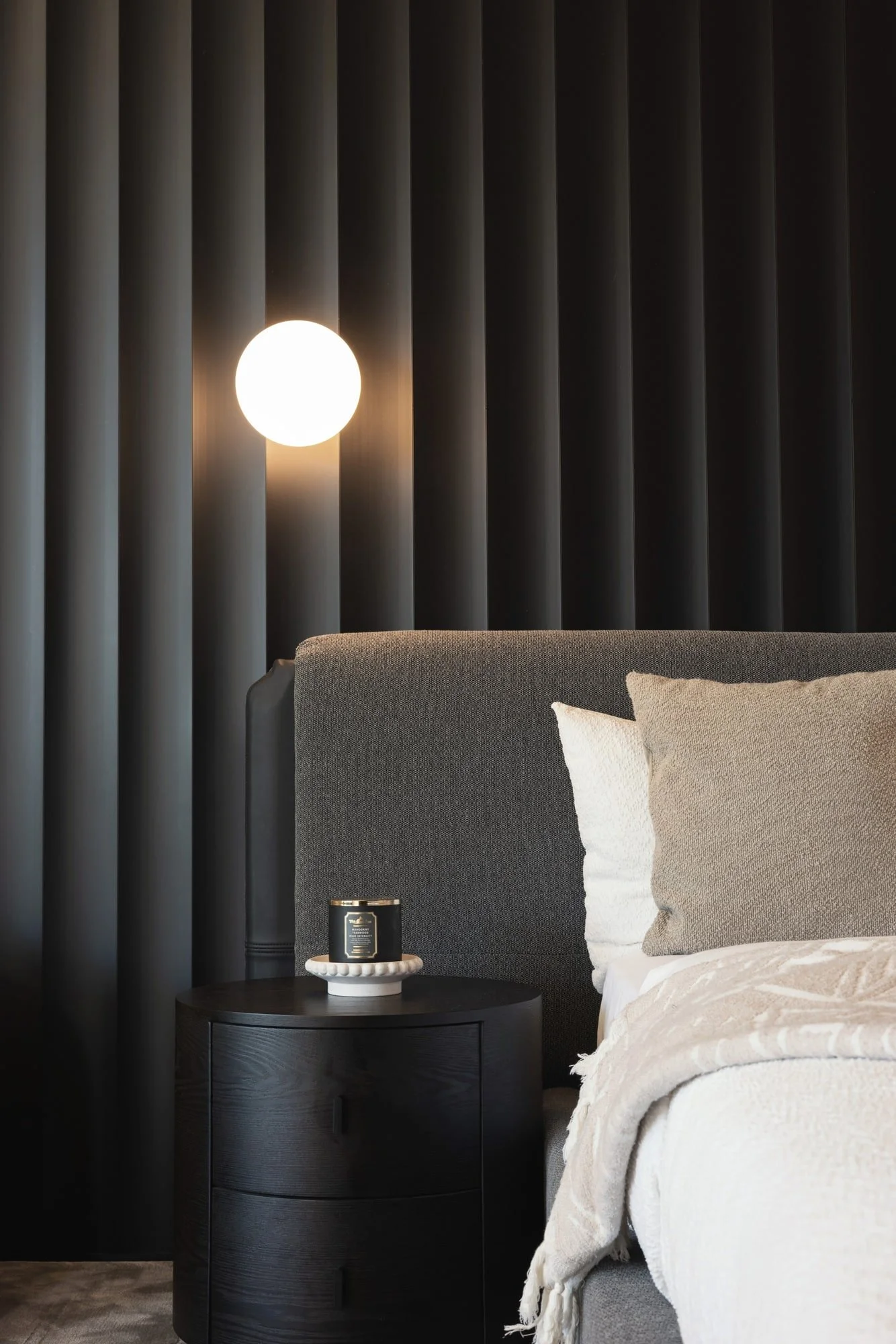 Bedroom detail with globe wall light and dark timber panels