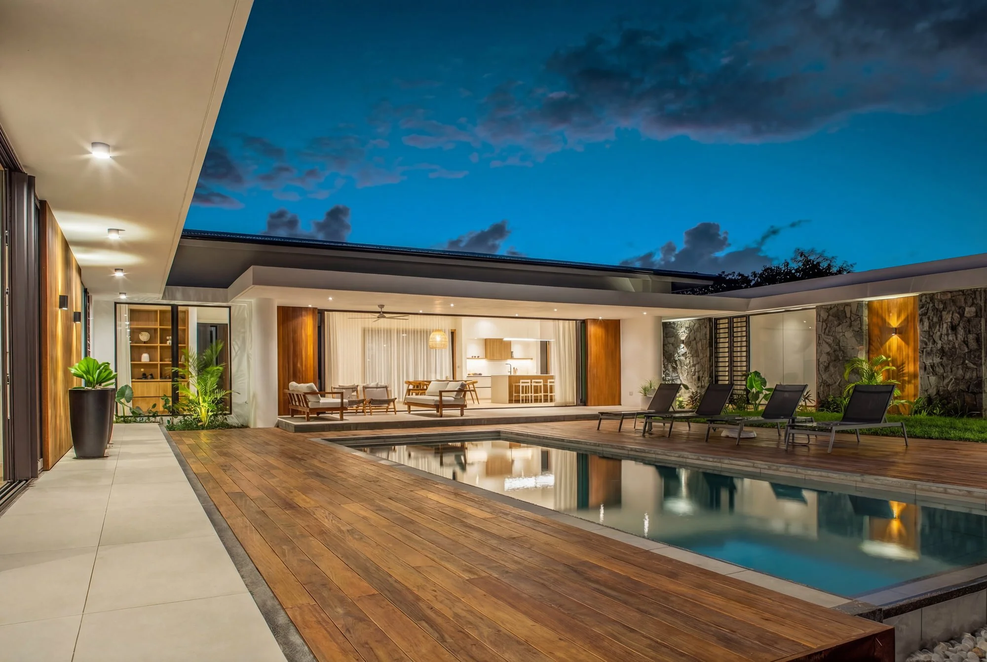 Une maison moderne avec une piscine, un espace extérieur avec mobilier, et un ciel crépusculaire étoilé.