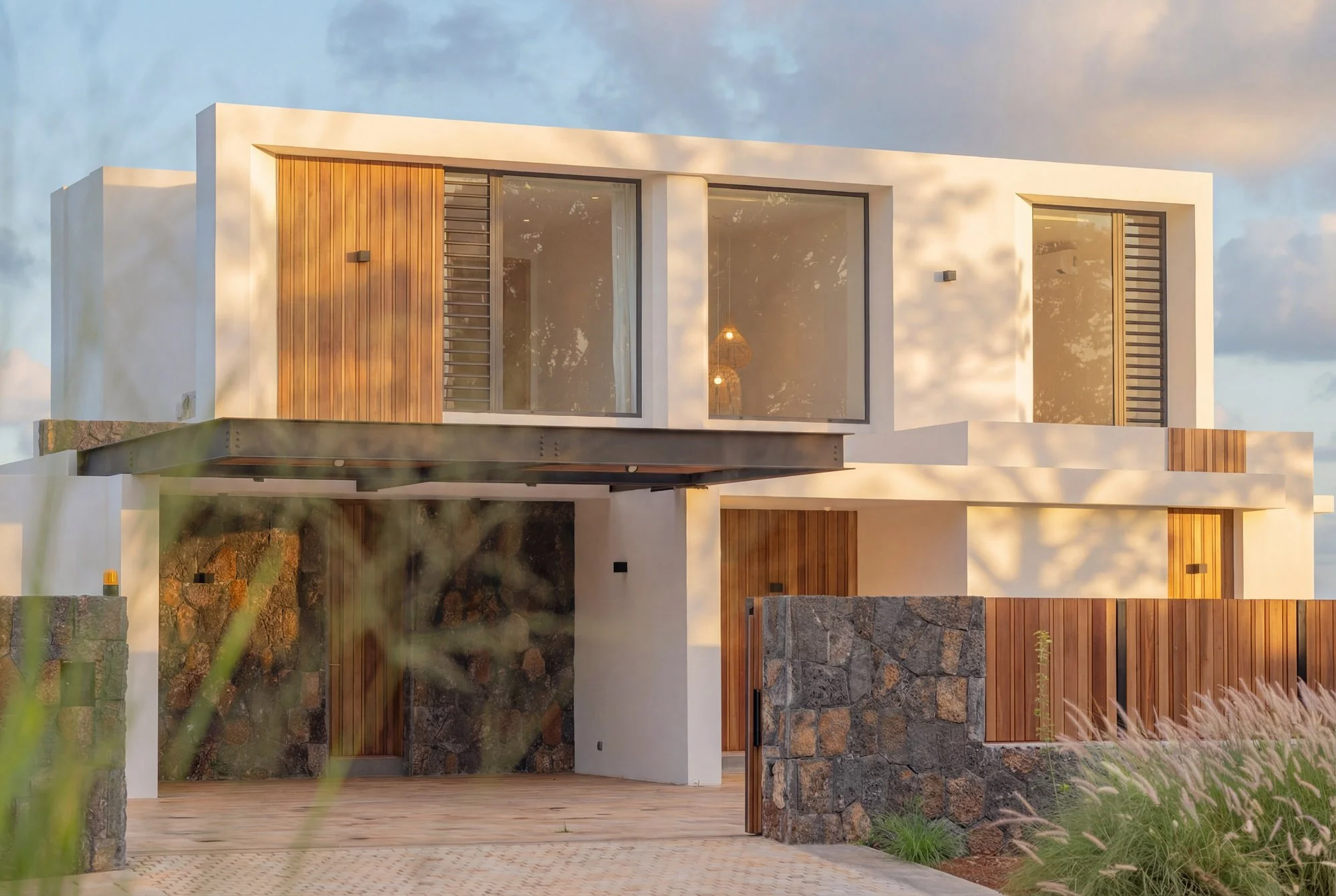 Façade moderne en pierre, bois et verre d'une maison contemporaine, avec un porche et un espace extérieur pavé.