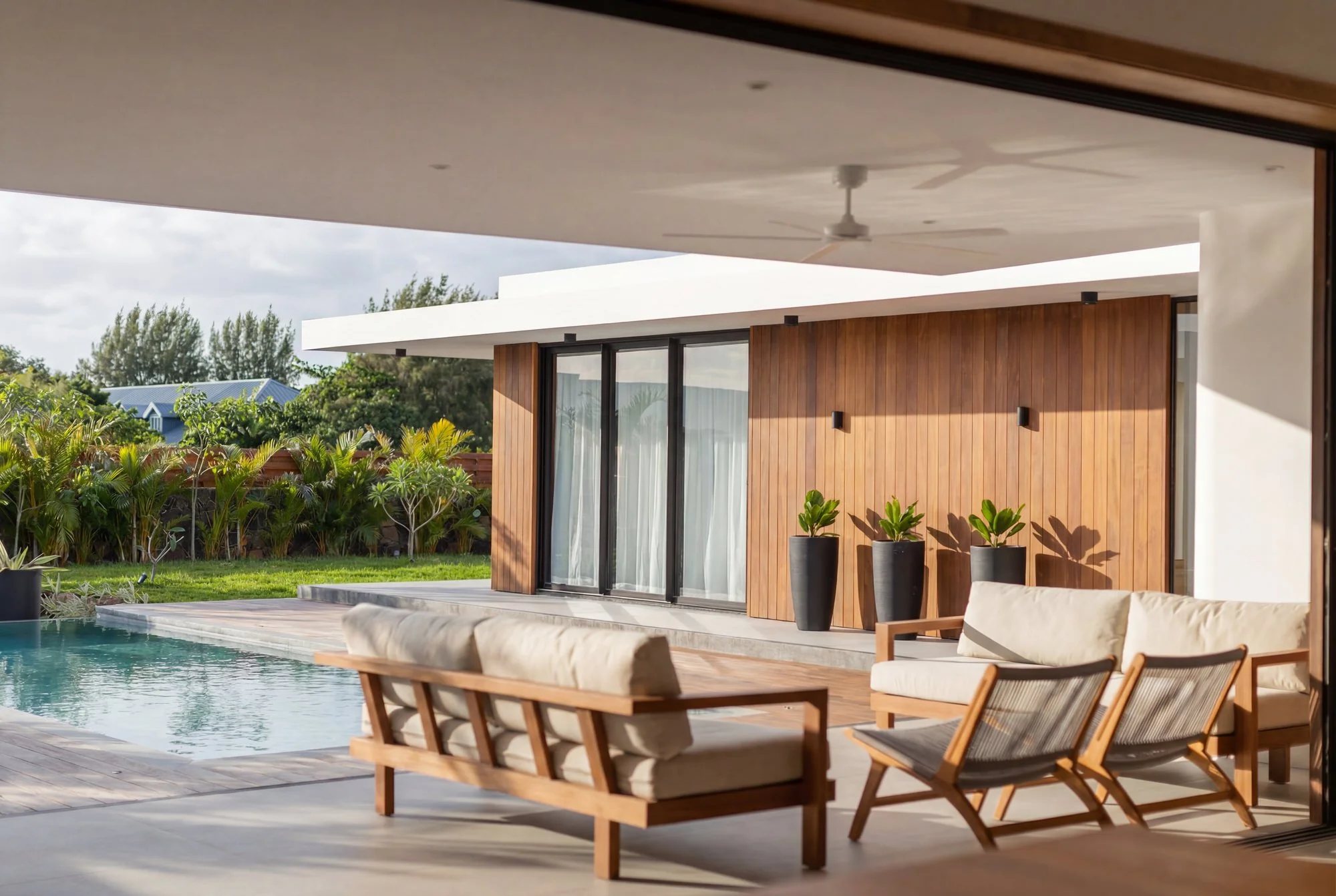 Une terrasse moderne avec mobilier en bois, un canapé beige, plusieurs chaises avec coussins, une piscine, des plantes en pot, et une façade en bois avec de grandes fenêtres, sous un plafond ombragé.