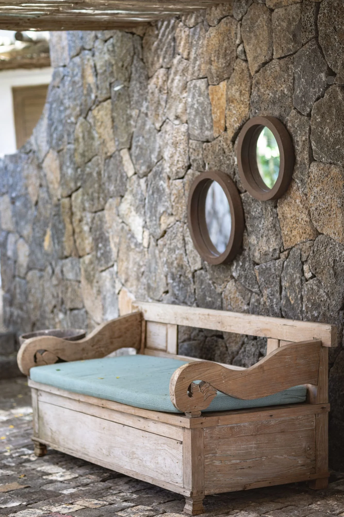 Rustic timber bench and circular mirrors against a volcanic stone wall