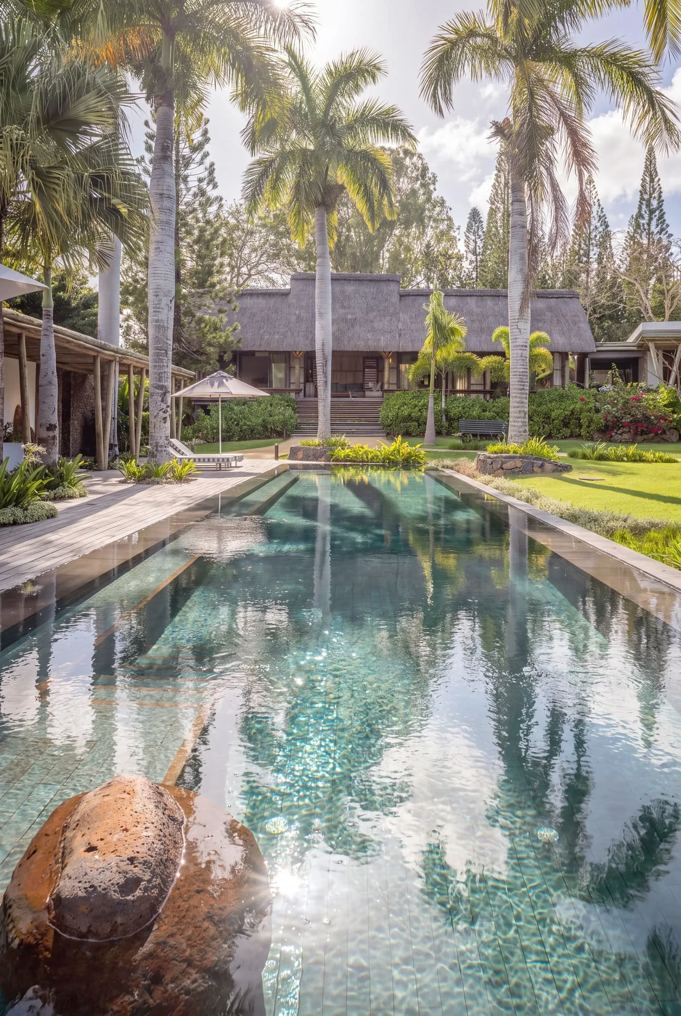 Long swimming pool reflecting the villa and its tropical garden