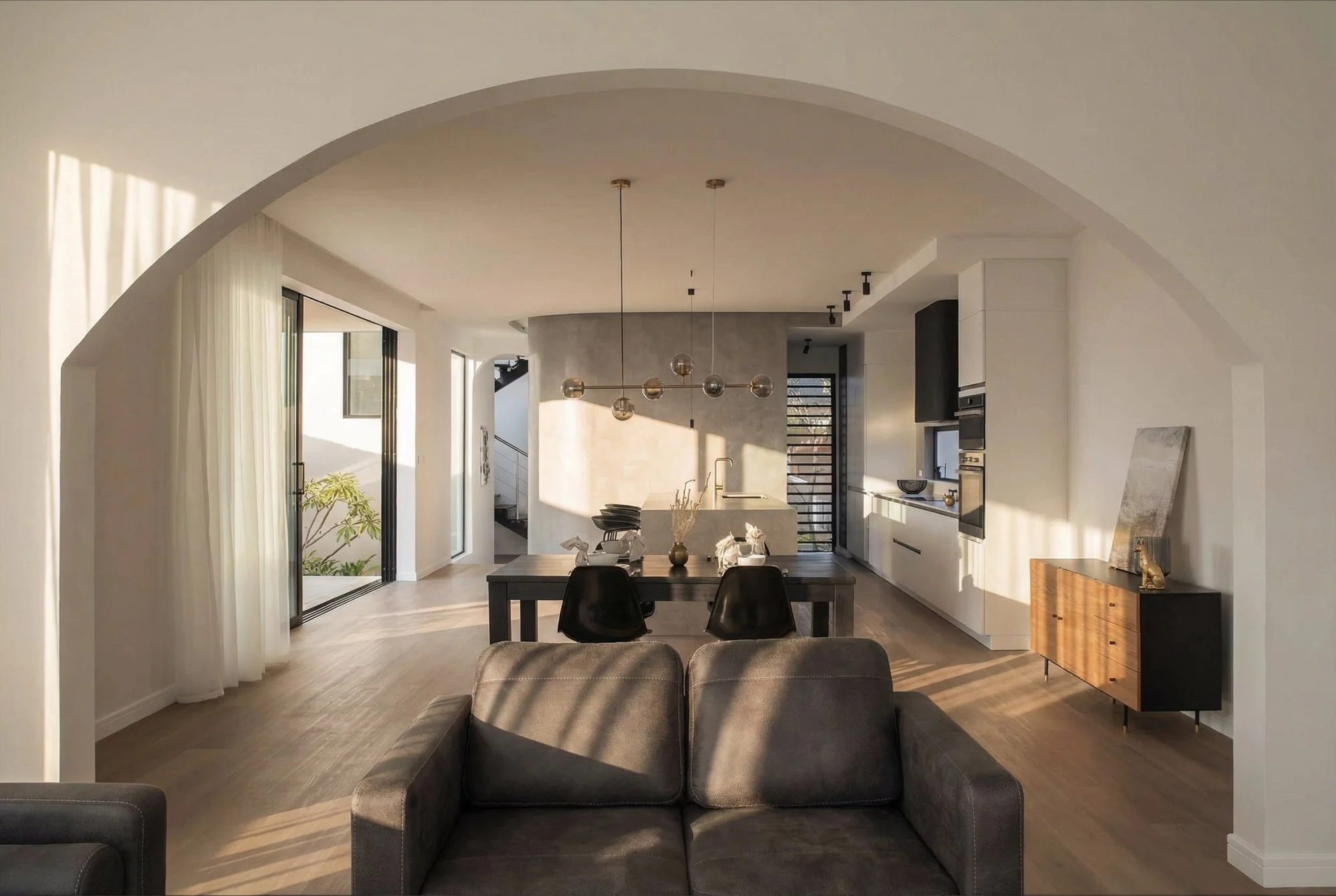Intérieur moderne d'une maison avec salon, table à manger, cuisine ouverte, grande porte-fenêtre, lumière naturelle, décor minimaliste.