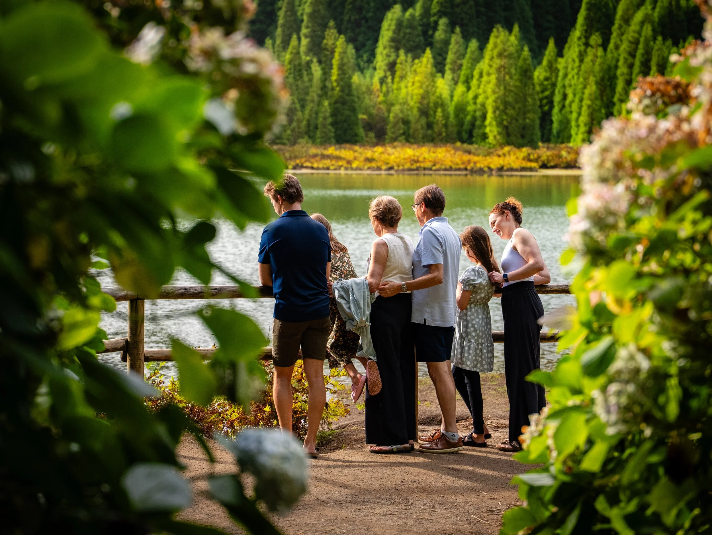 Family enjoying a quiet moment by a lake, framed by green leaves in São Miguel, Azores