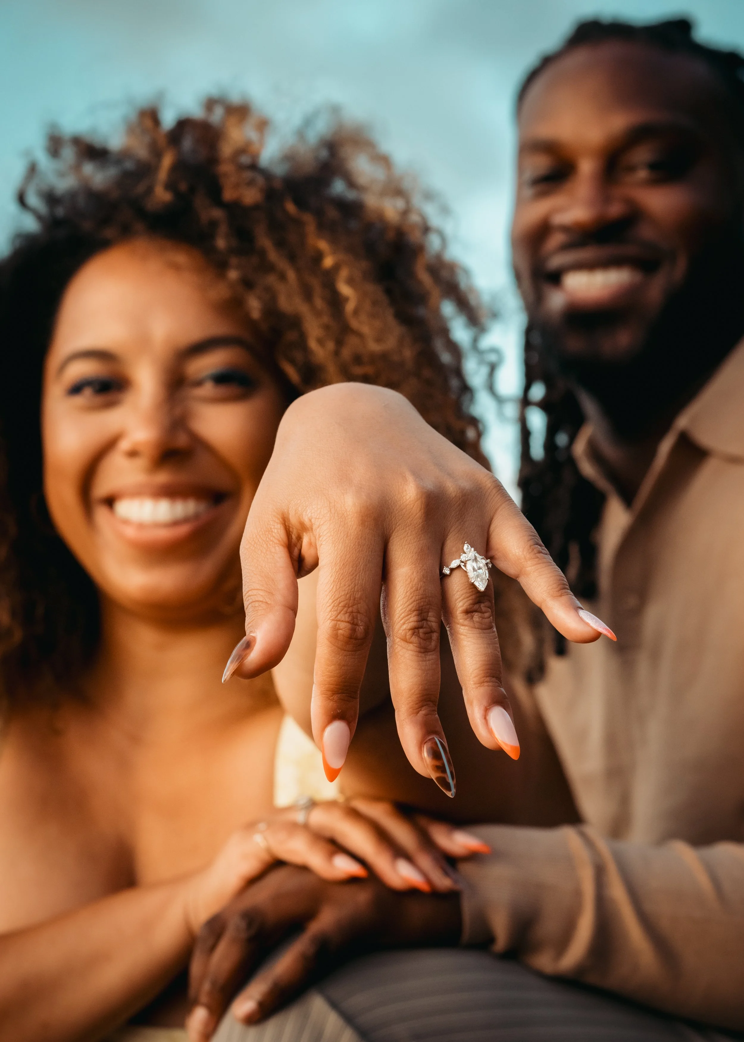 Engagement ring close-up during surprise proposal in the Azores with couple smiling in the background