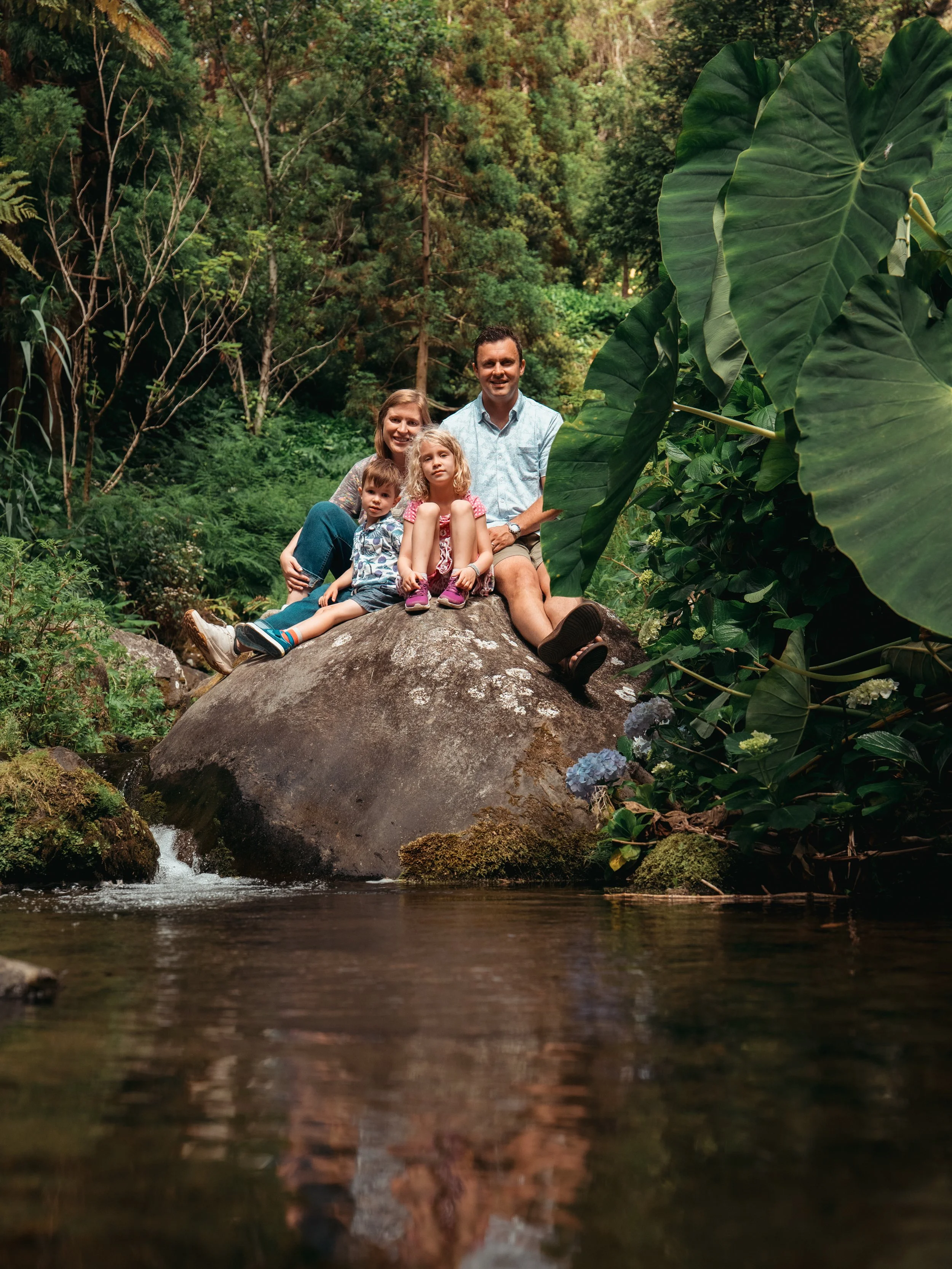 Family sitting on a large rock surrounded by lush green vegetation in São Miguel, Azores