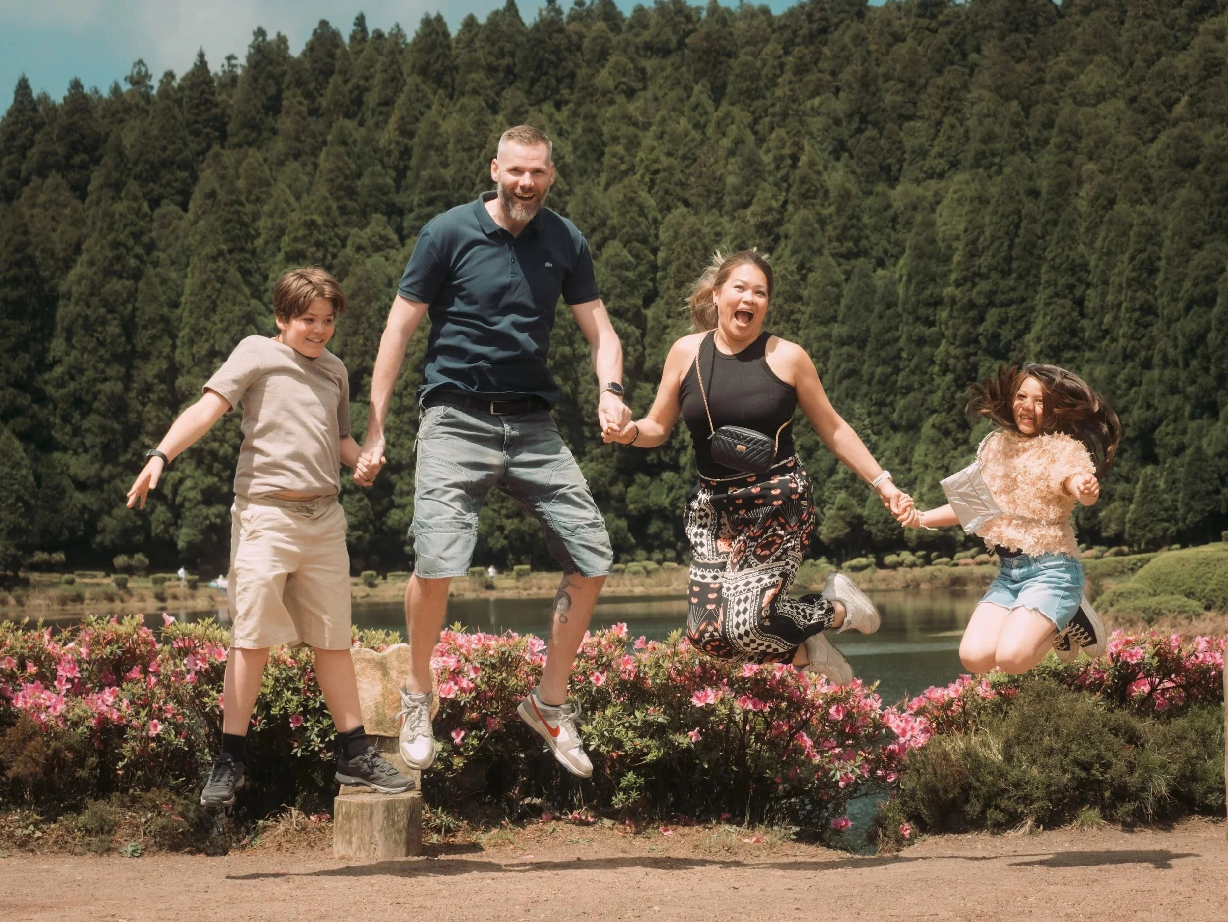 Happy family jumping during a private tour in São Miguel - Azores with a scenic lake and forest background