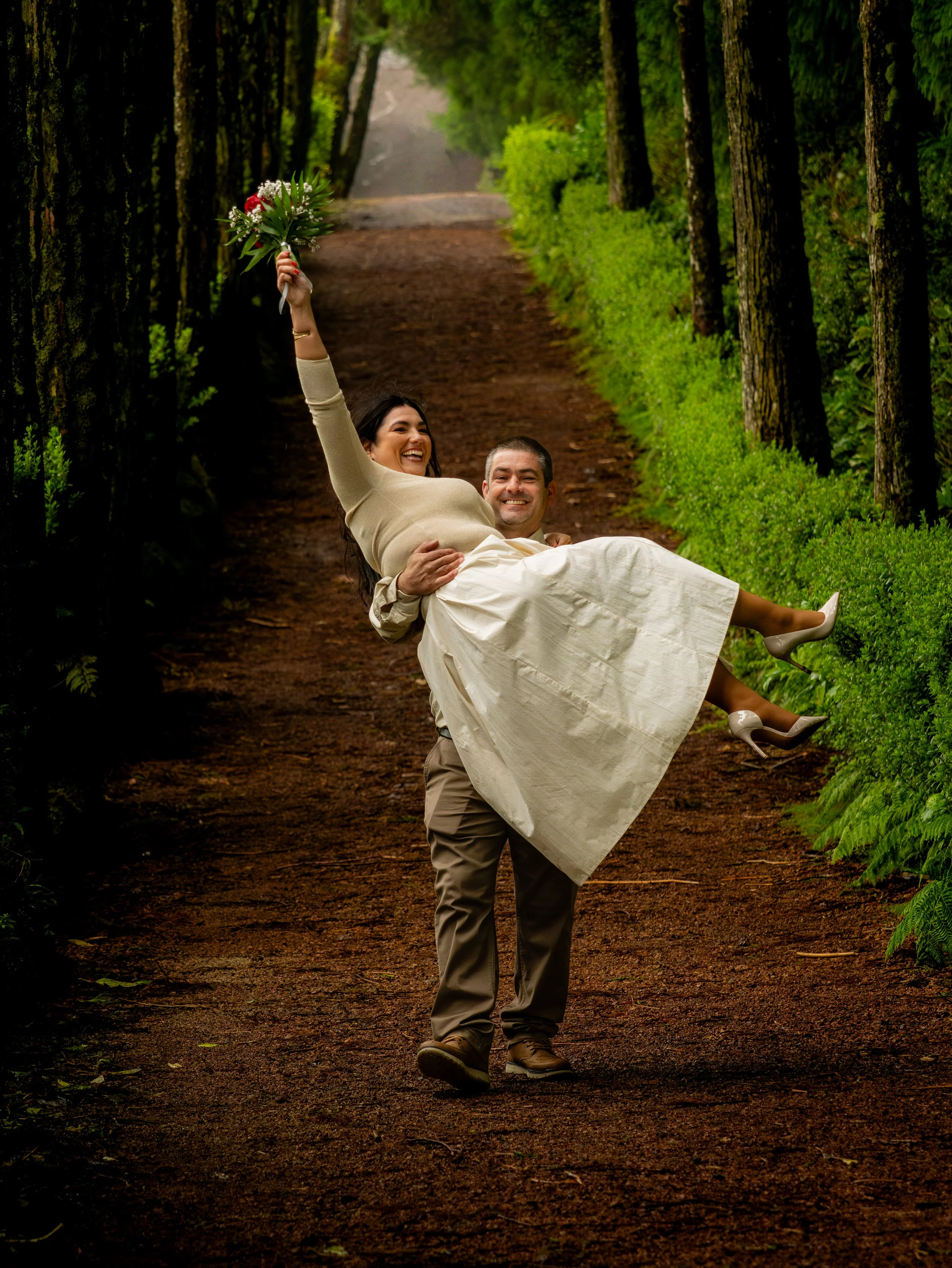 Couple celebrating their elopement on a forest path in São Miguel, Azores, with the bride holding a bouquet and smiling