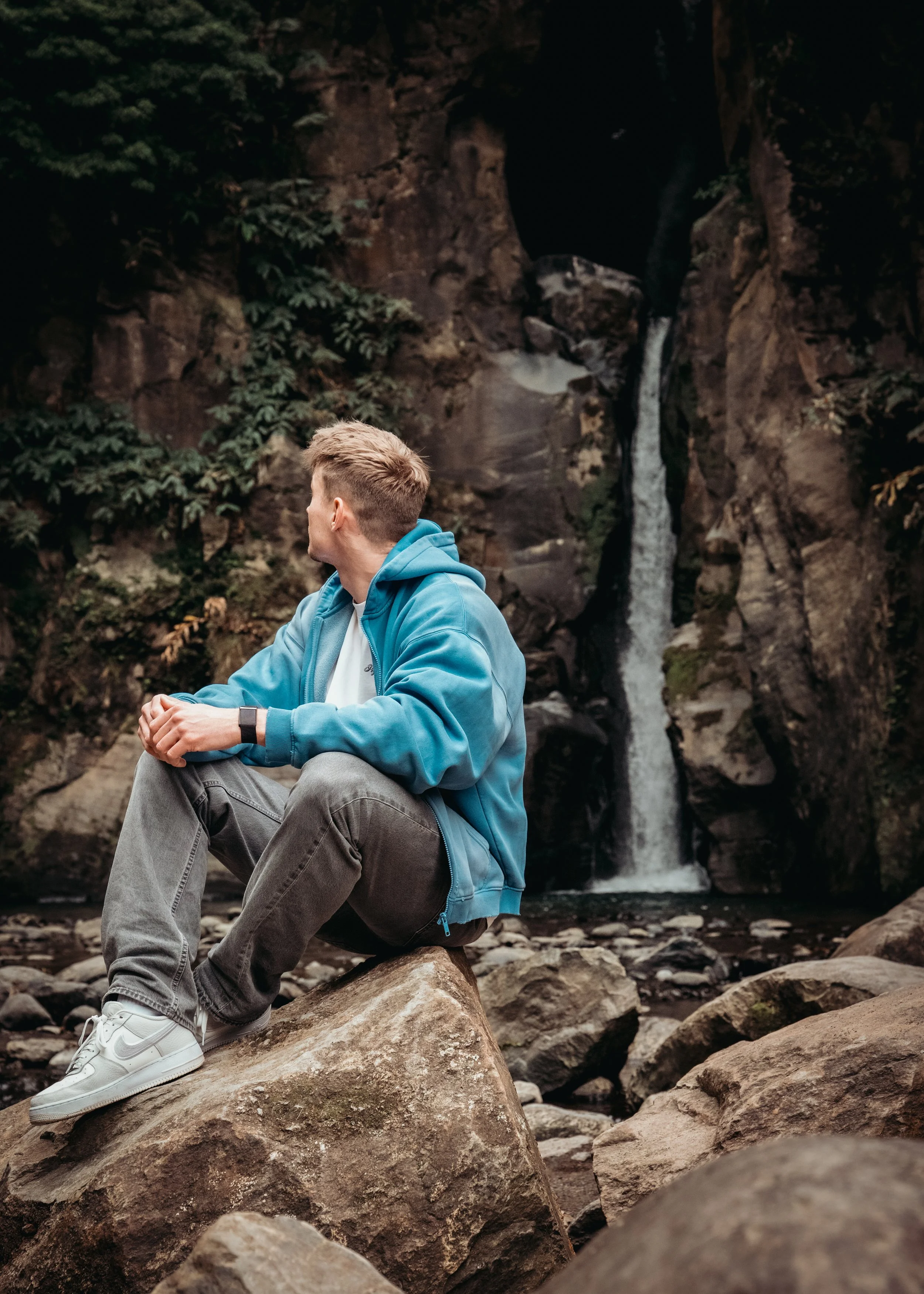 A visitor sitting on rocks in front of a hidden waterfall in São Miguel Island, Azores during a photo tour with a local Azores photographer.