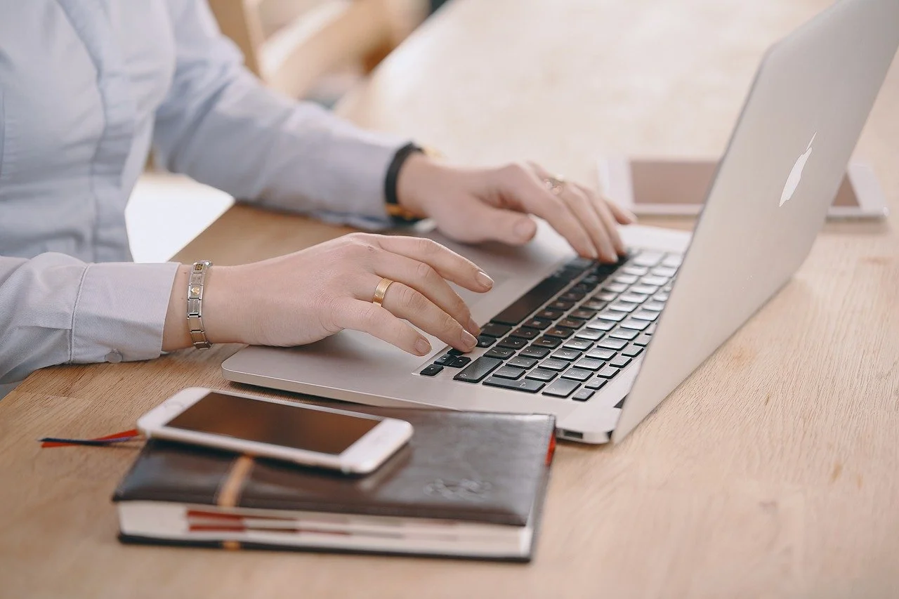 Person typing on a laptop with a notebook and smartphone on a desk.