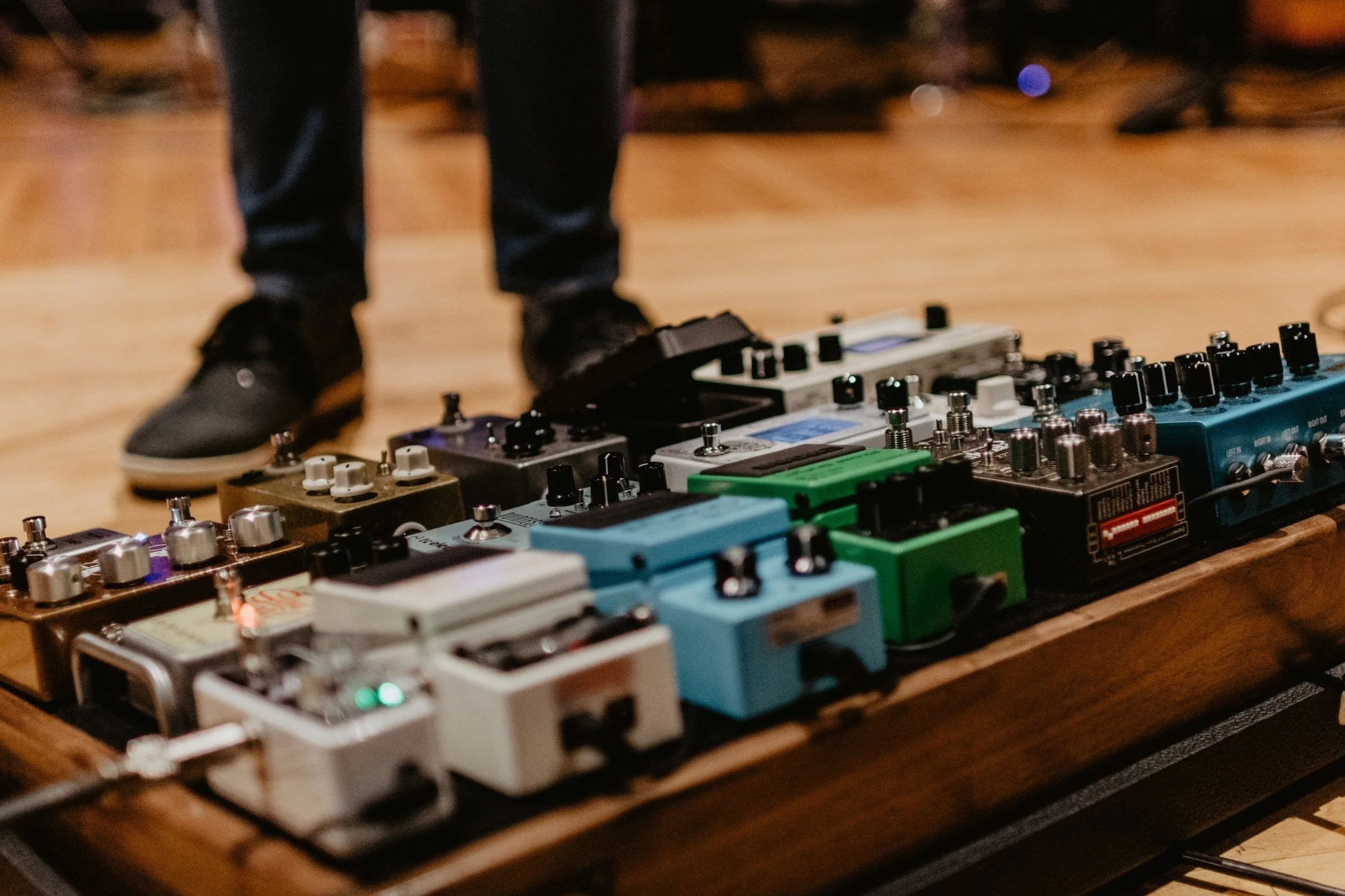 Guitar effects pedals on a pedalboard with person standing.