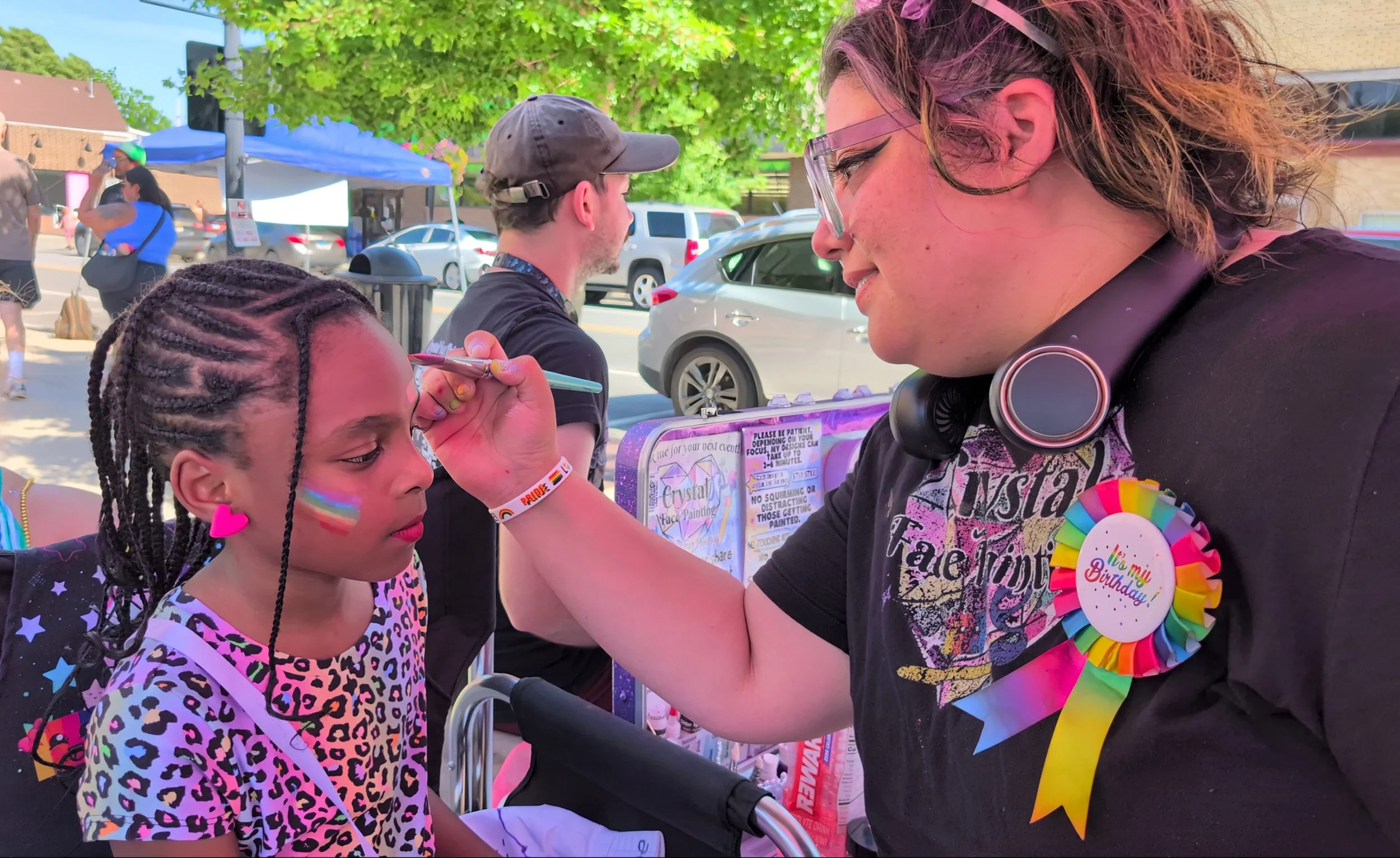 a man in a red shirt and grey hat holding a blackboard with "Free Face Paint 3-6 pm Tips Welcome" written on it