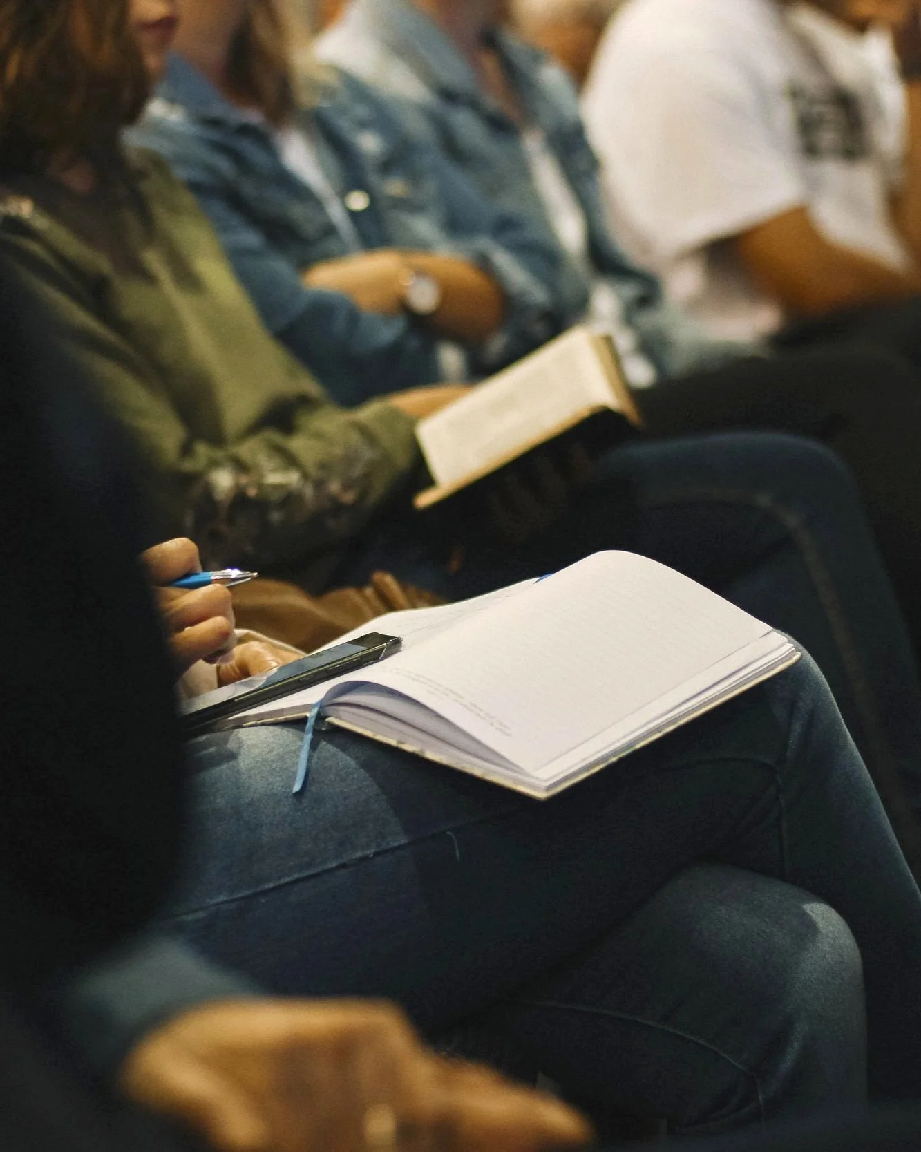 People sitting in a row, some holding notebooks or using smartphones, attending an education session.
