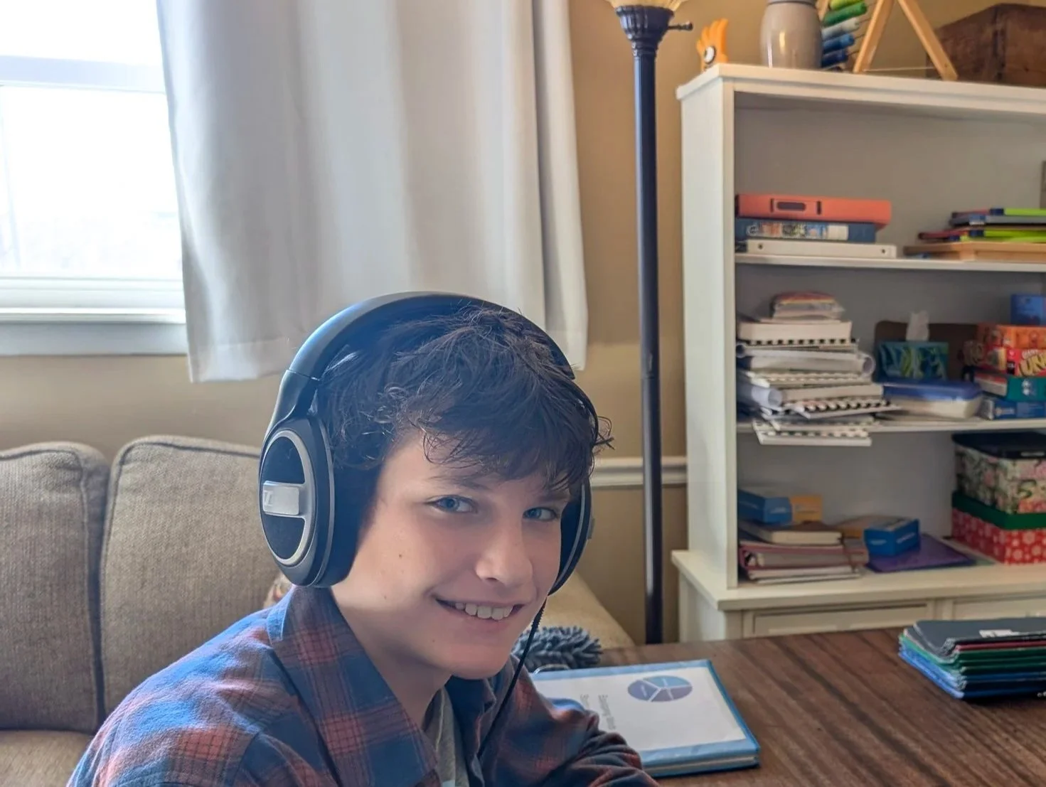 A teenager with headphones and a woman sitting at a table playing a card game. The room has a bookshelf with games and books.