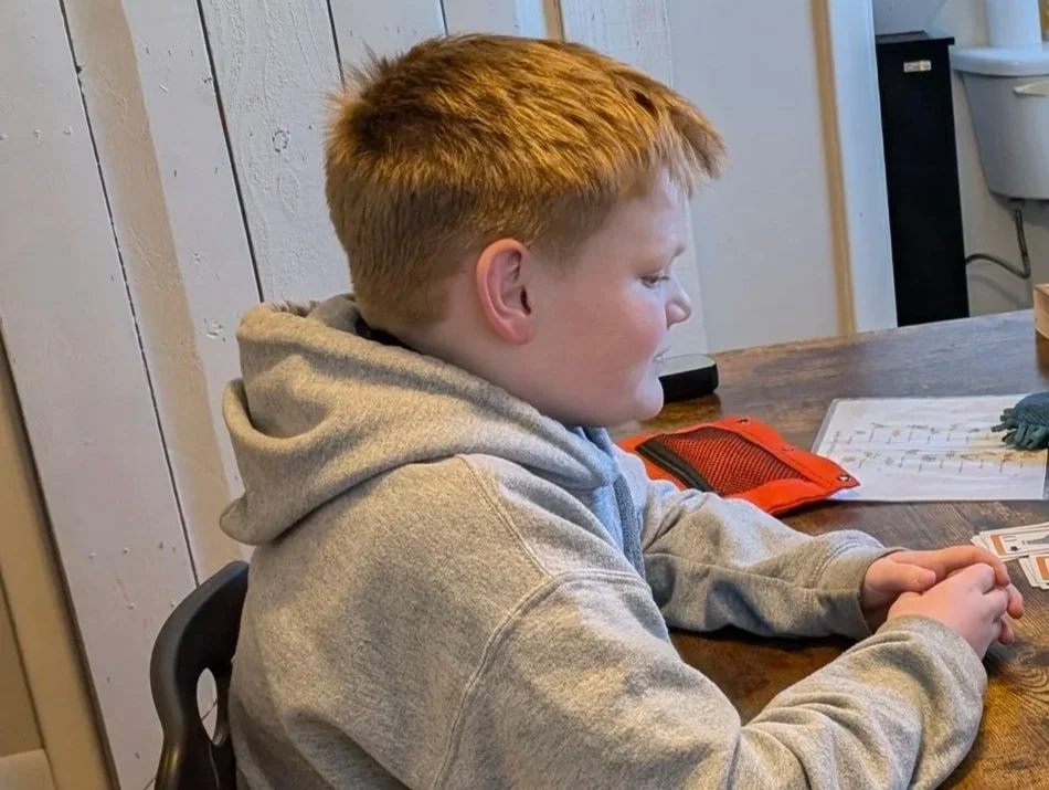 A child and an adult engaged in an educational activity with cards at a desk in a home or office setting.