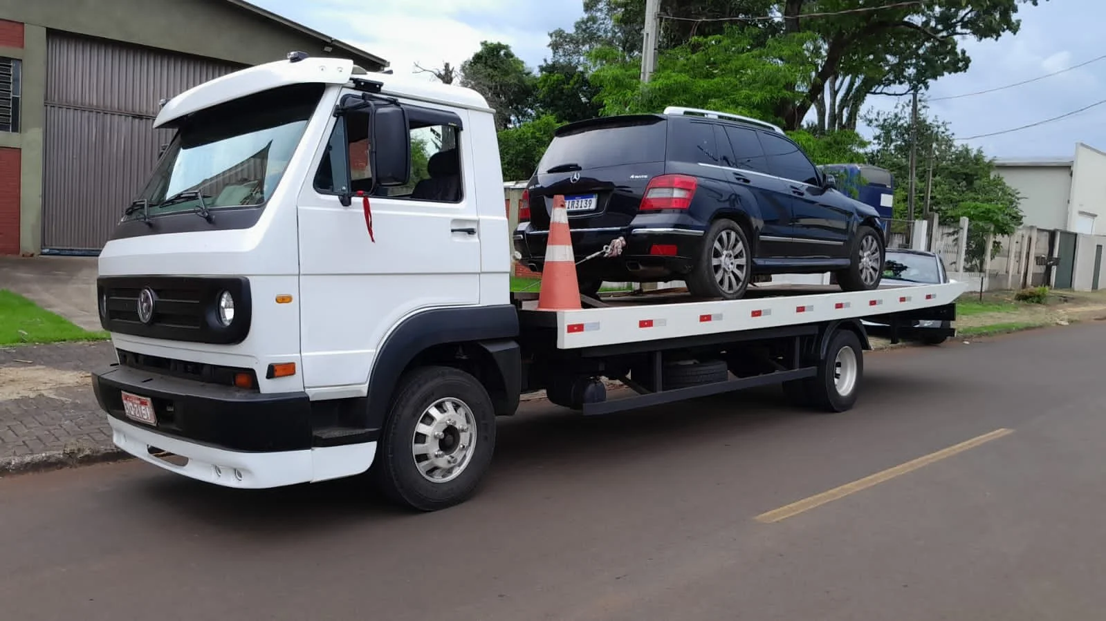 Caminhão AmGuinchos, transportando um carro preto, com cones de trânsito e corrente de segurança.