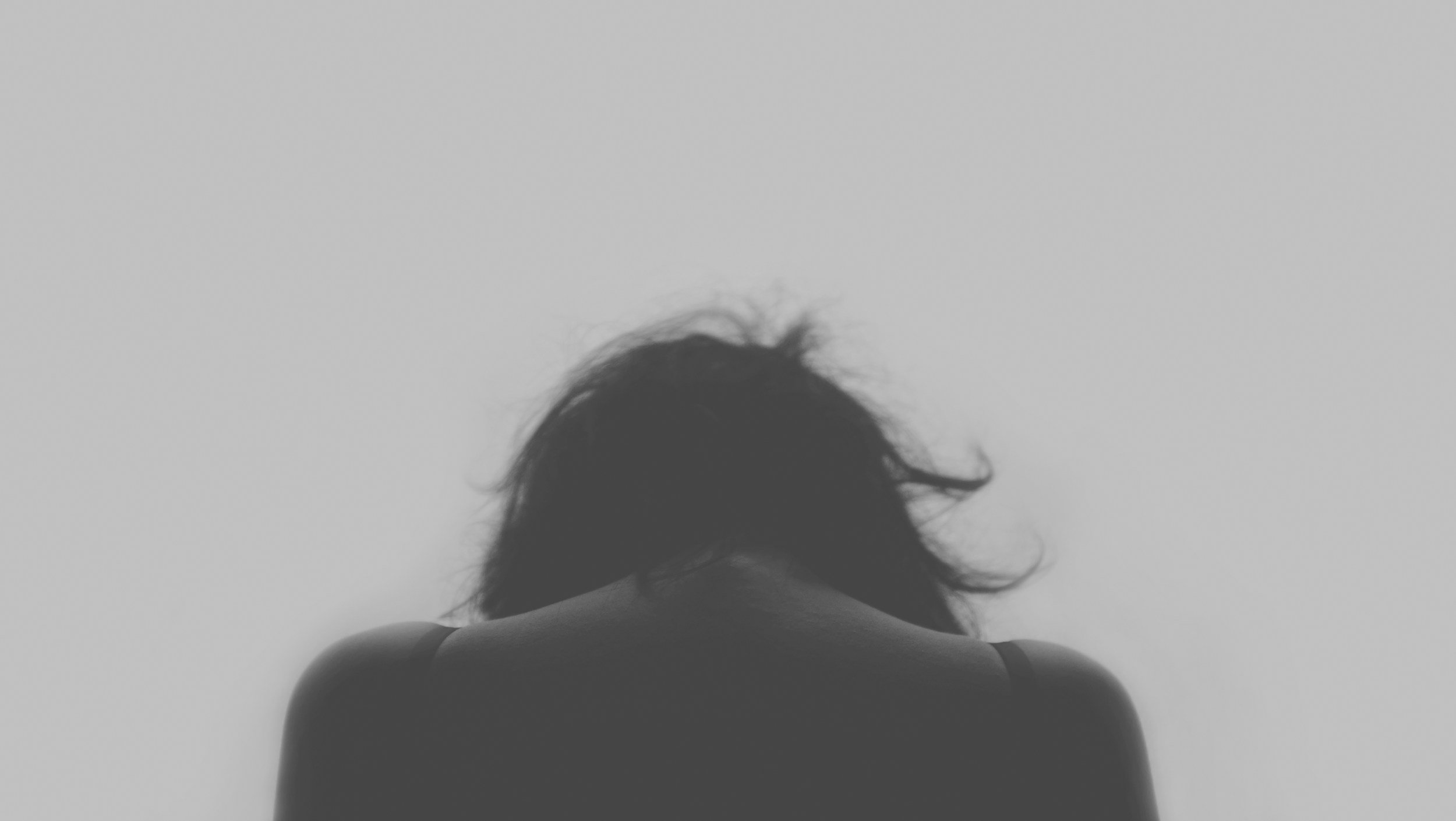 A black and white photo of the back of a woman with her head down showing how burnout and depression can make women in Greenville, SC feel before online therapy with Emilea Richardson