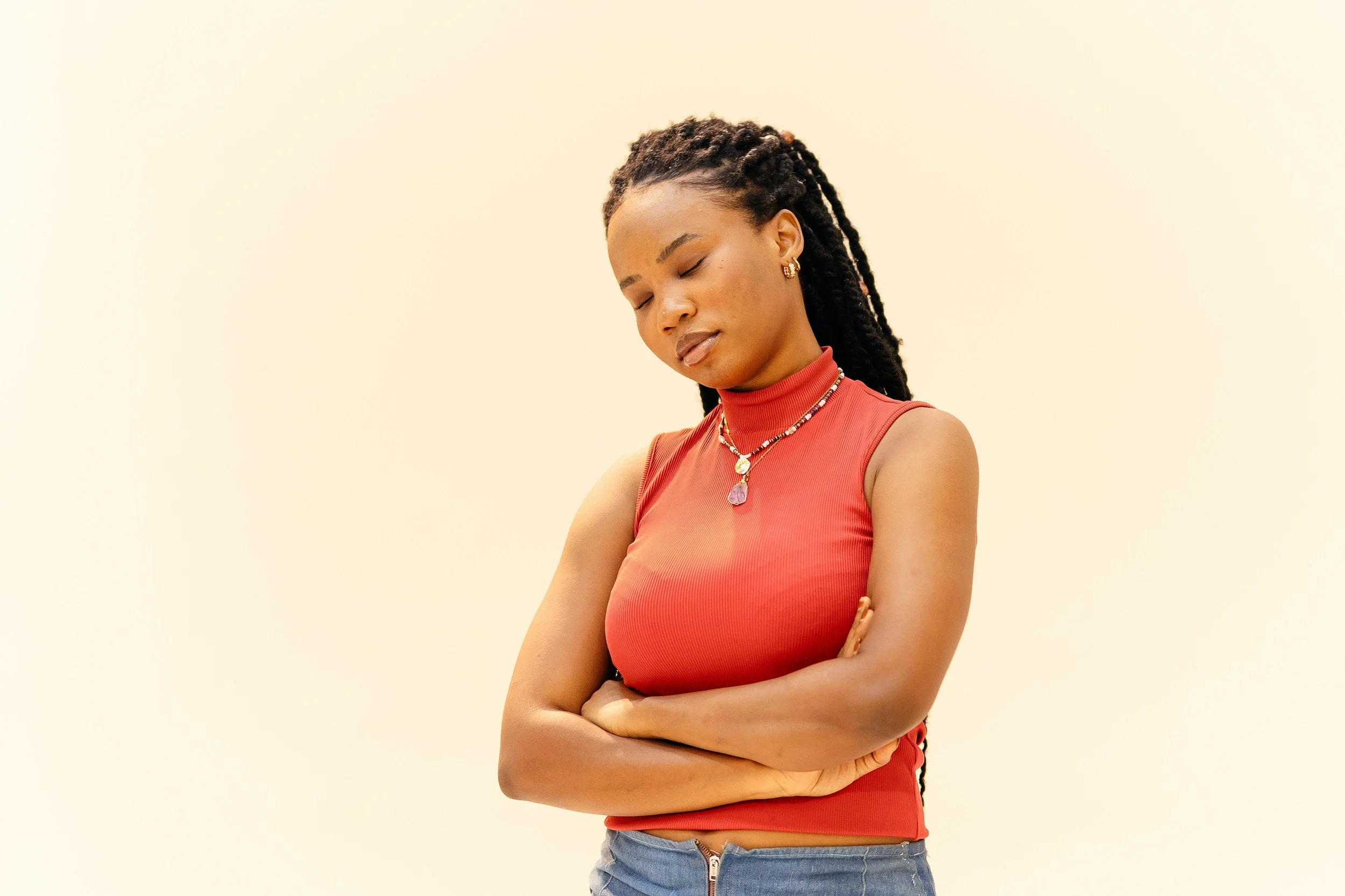 A black woman wearing an orange top is standing with her arms folded and her eyes are closed with a relaxed face, showing how mindfulness and online anxiety therapy in Greenville, SC can reduce anxiety for women.