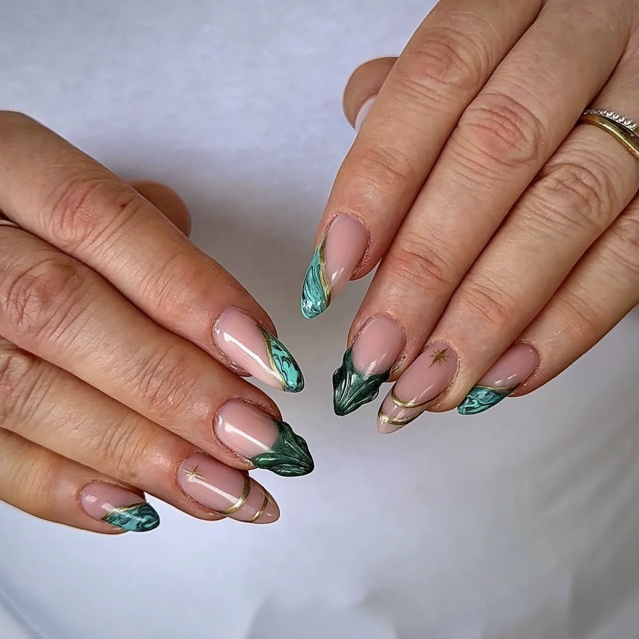 Close-up of hands with manicured nails featuring green and blue marble design, gold accents, and small star decals.