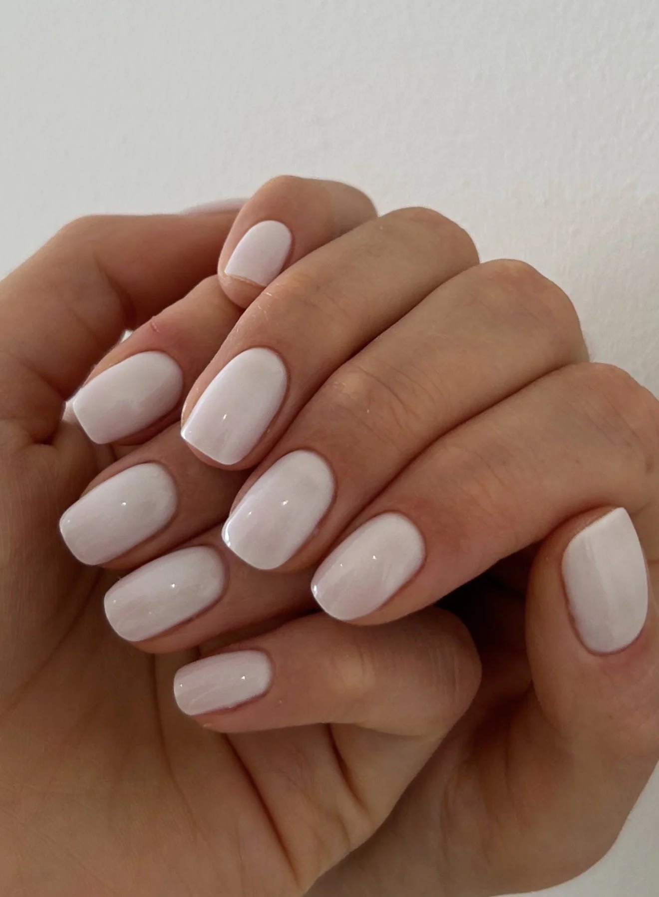 Close-up of a hand with manicured nails painted in a glossy white color, with a plain white background.