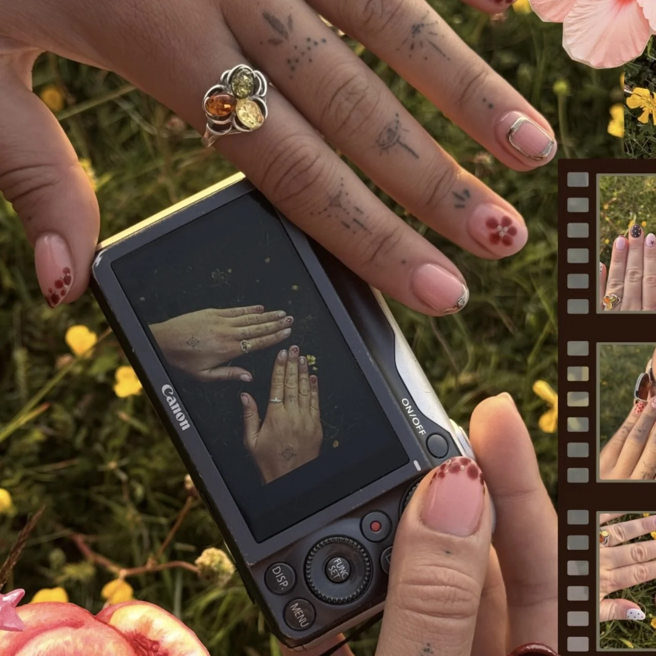 Close-up of a person's hand with intricate tattoos and colorful rings, taking a photo of their other hand with a smartphone. The other hand has decorated nails with red flower designs. The background features yellow flowers and greenery, with a parti