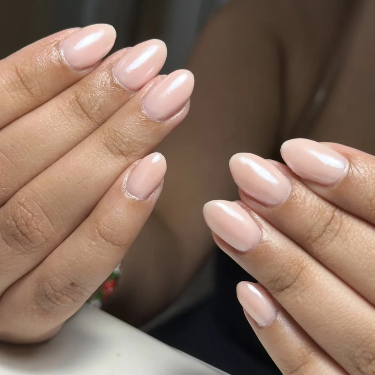Close-up of two hands with natural, well-manicured nails, showing a subtle glossy, light pink nail polish and smooth skin.