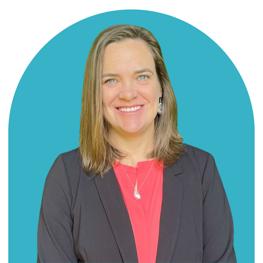A professional woman with shoulder-length blonde hair, smiling, wearing a black blazer and coral blouse, with a necklace and earrings, against a blue background.
